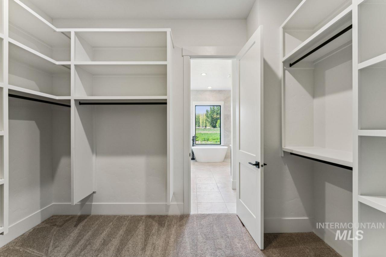 Walk-in closet with white built-in shelving, opening onto a tiled bathroom with a freestanding tub.