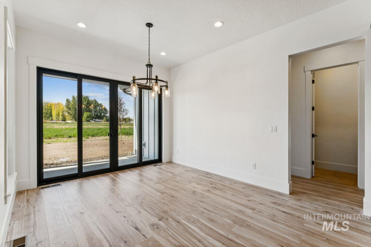Vacant dining room with a dark chandelier and sliding glass doors overlooking fields and autumn trees.