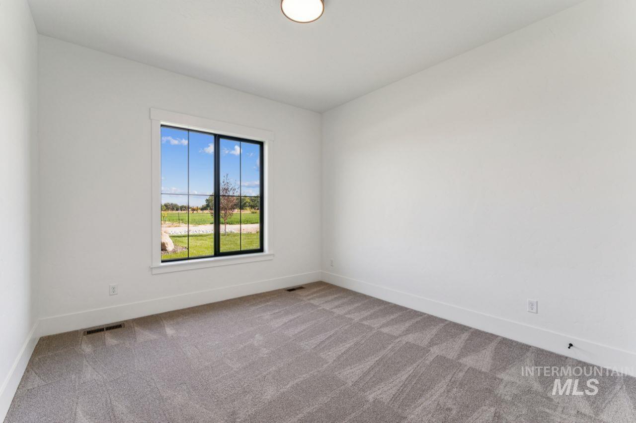 Empty bedroom with gray carpet and a large window overlooking a green lawn.