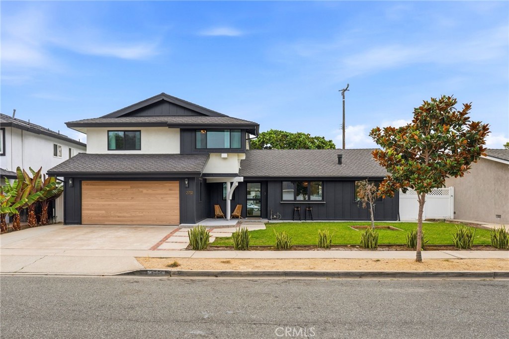 Two-story modern home with dark siding, a wood garage door, and a front lawn.