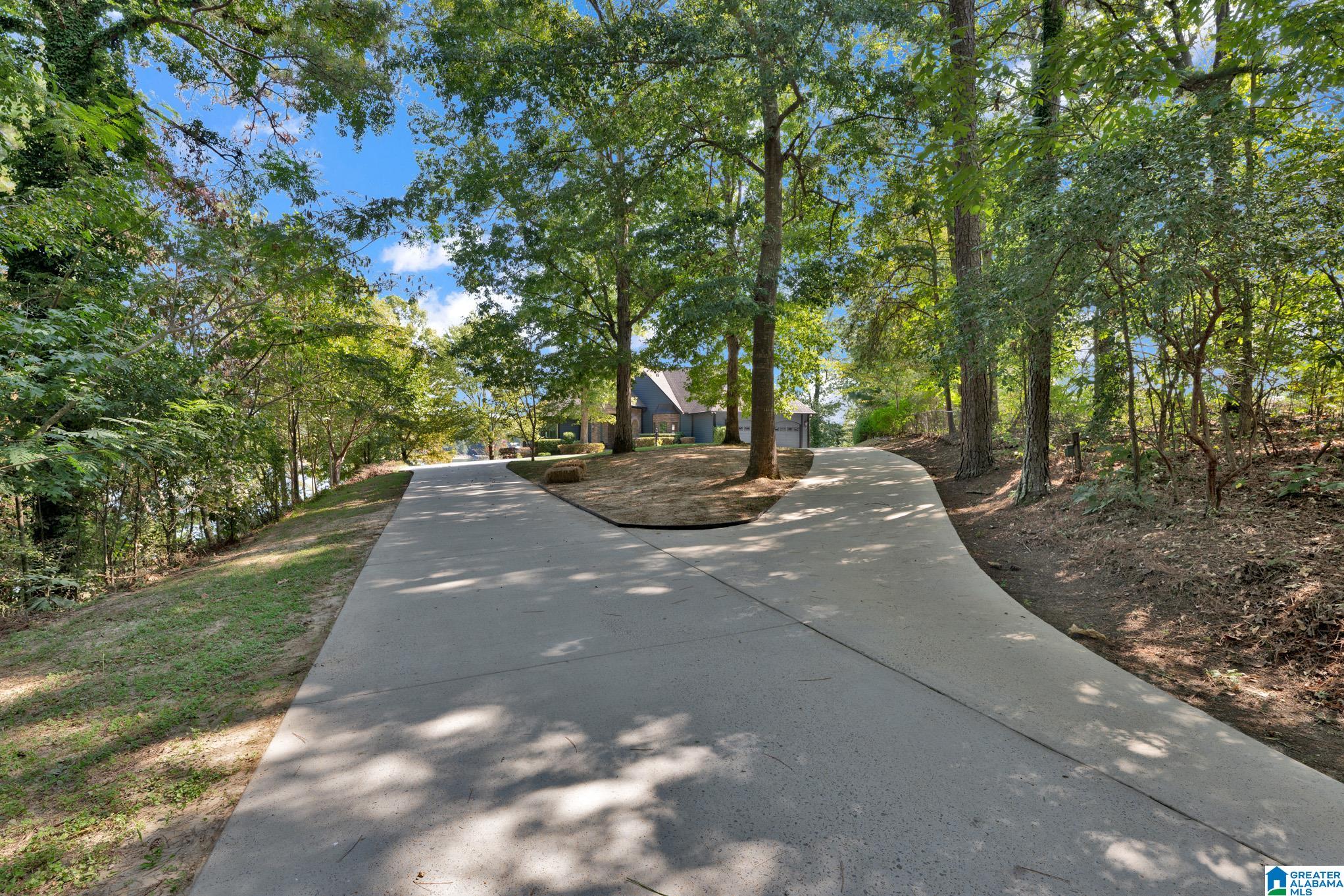 House at the end of a curving concrete driveway, surrounded by mature trees.