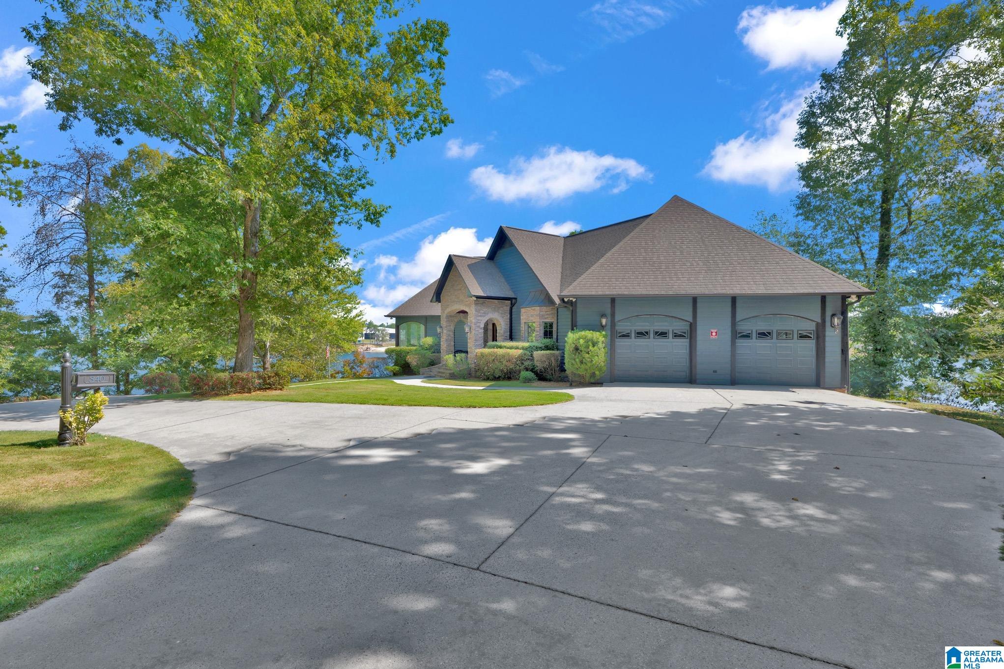 Gray-blue house with stone entry and two garage doors beside the water, framed by trees.