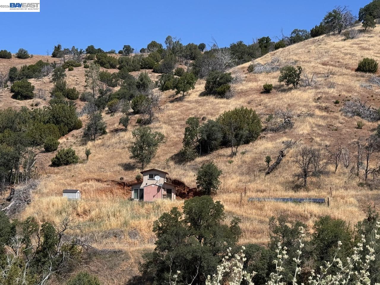 Dry grassy hillside acreage with scattered trees, a small outbuilding, and ground-mounted solar panels.