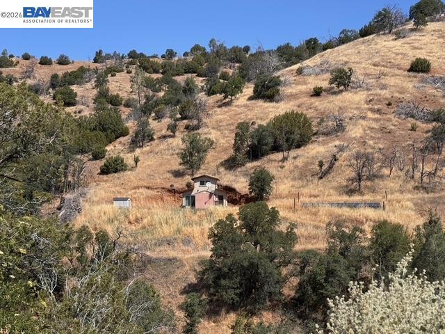 Rural hillside property with golden grass, scattered trees, fencing, and a small structure.