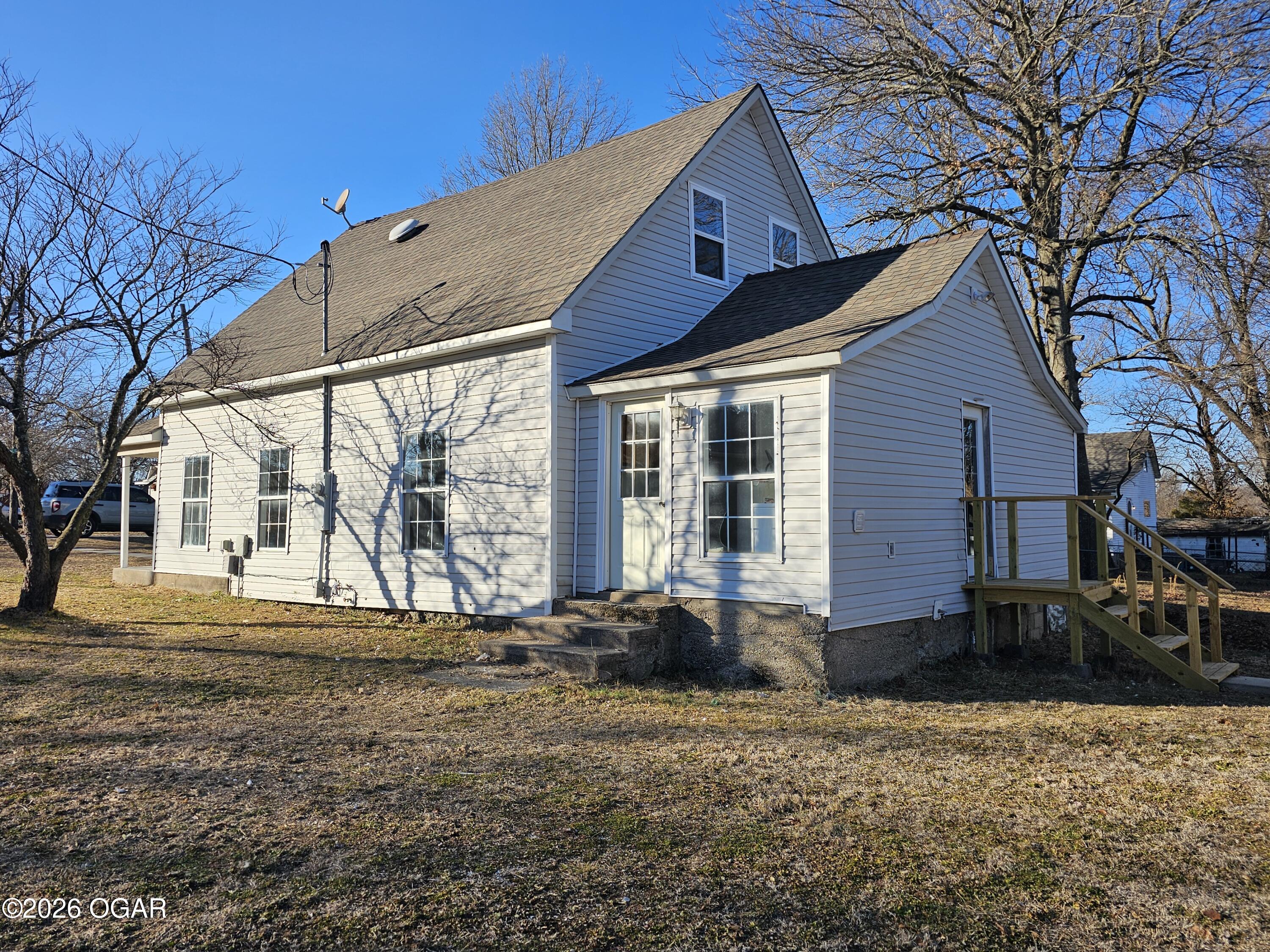 White two-story house with steep gables, a small wooden deck, and leafless trees.