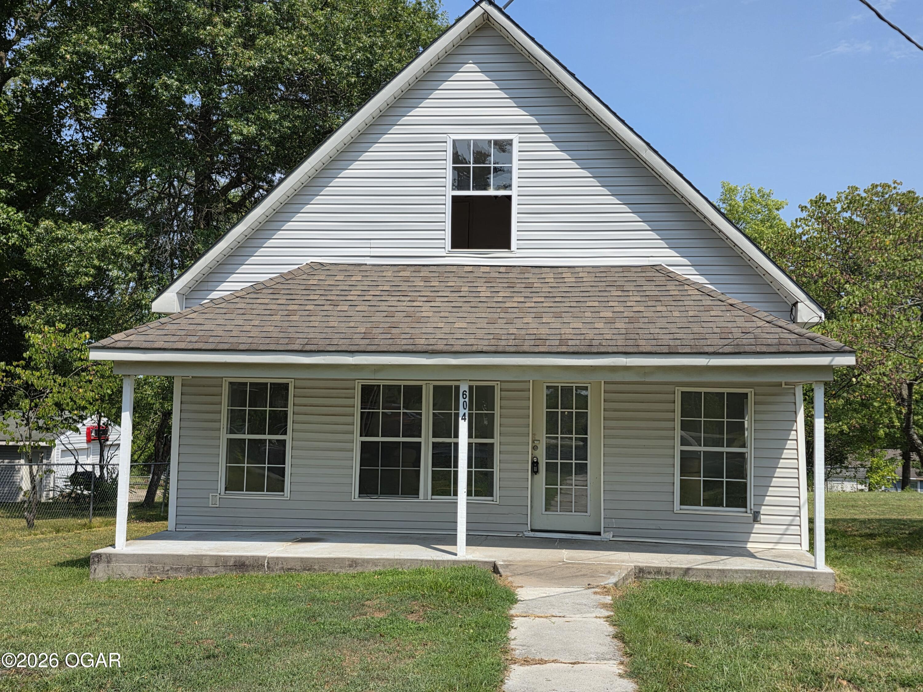 Gray-sided house with a steep front gable, covered porch, and concrete walkway.