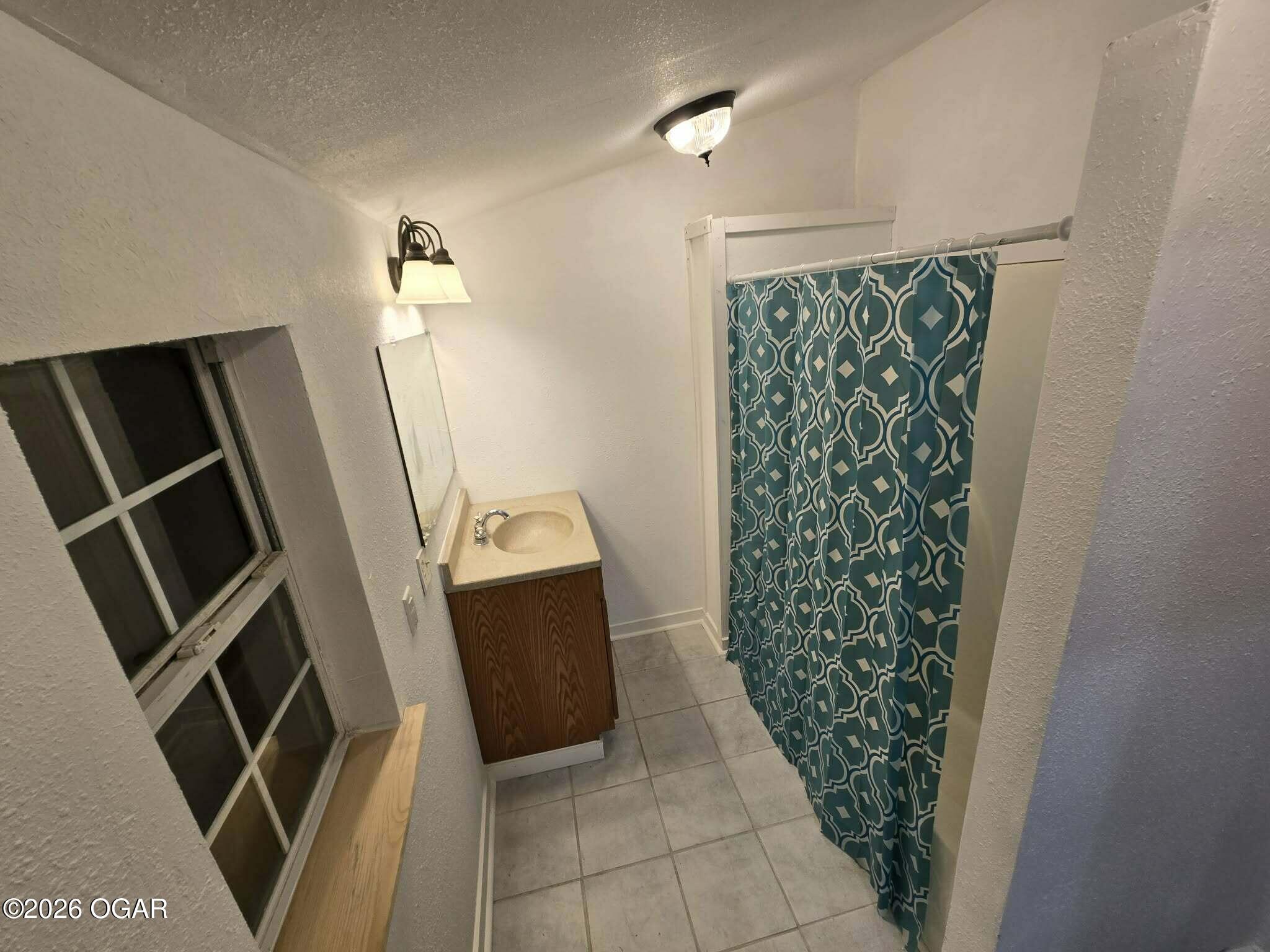 Bathroom with a wood-front vanity, tiled floor, and teal patterned shower curtain.