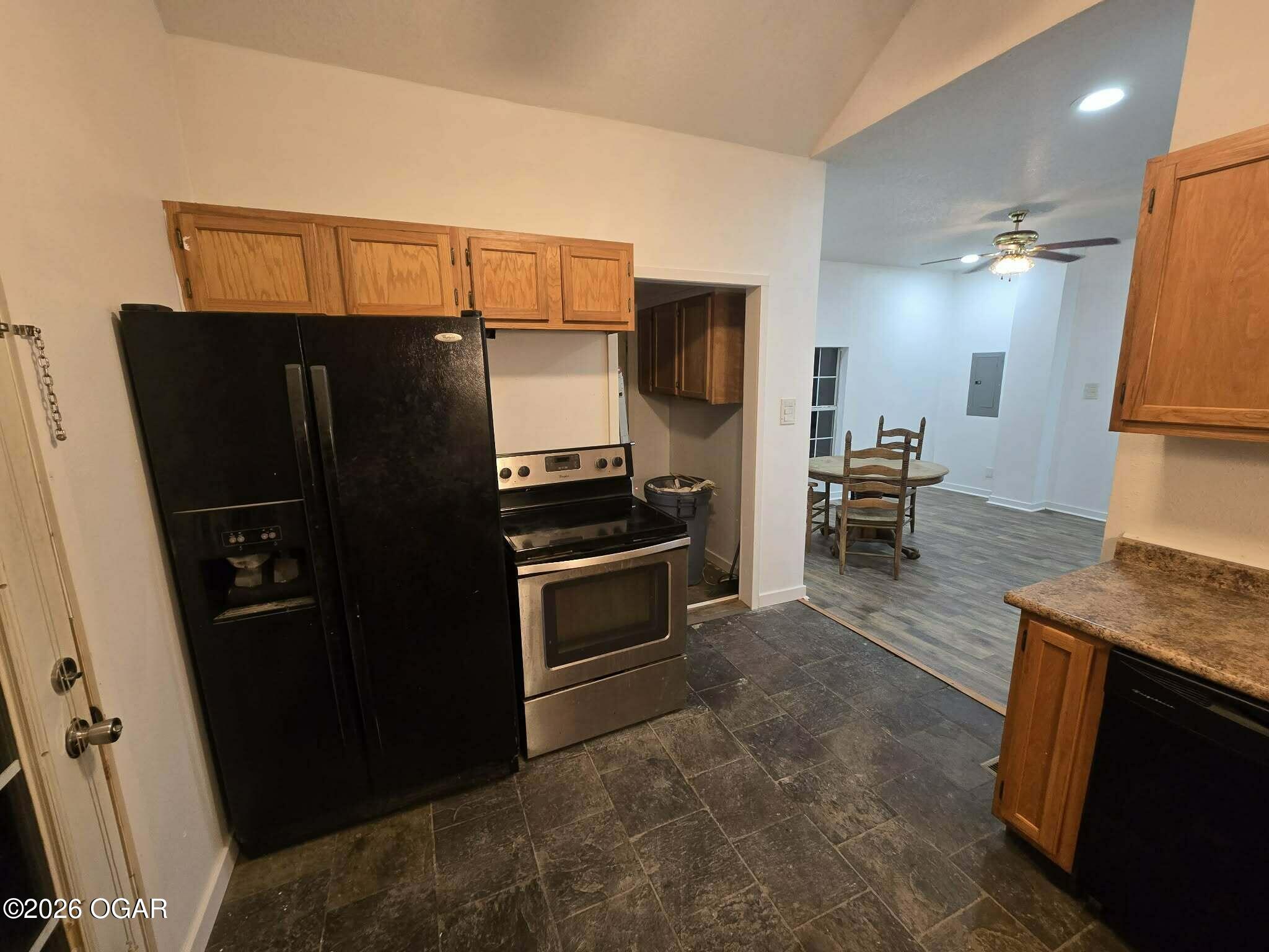 Kitchen with wood cabinets, black refrigerator, and range opening to a dining area.