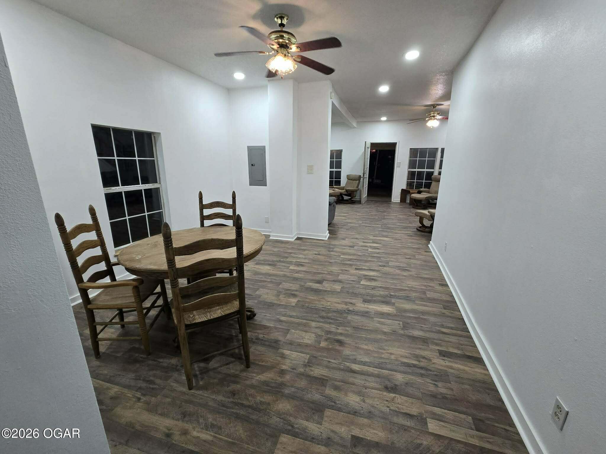 Open dining and living area with a round wooden table, recliners, dark flooring, and ceiling fans.