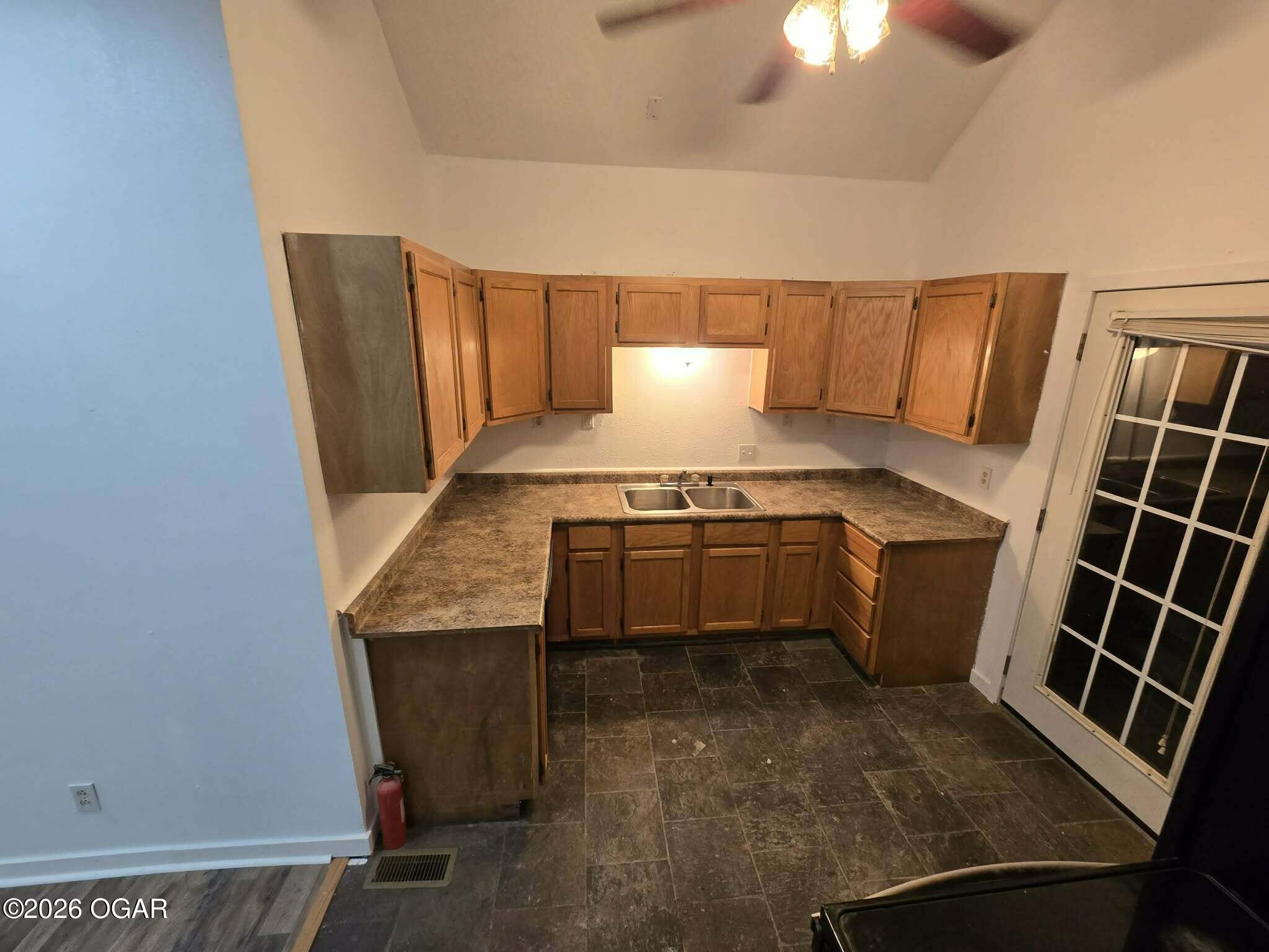 Kitchen with wooden cabinets, L-shaped counters, a double sink, and dark tile flooring.