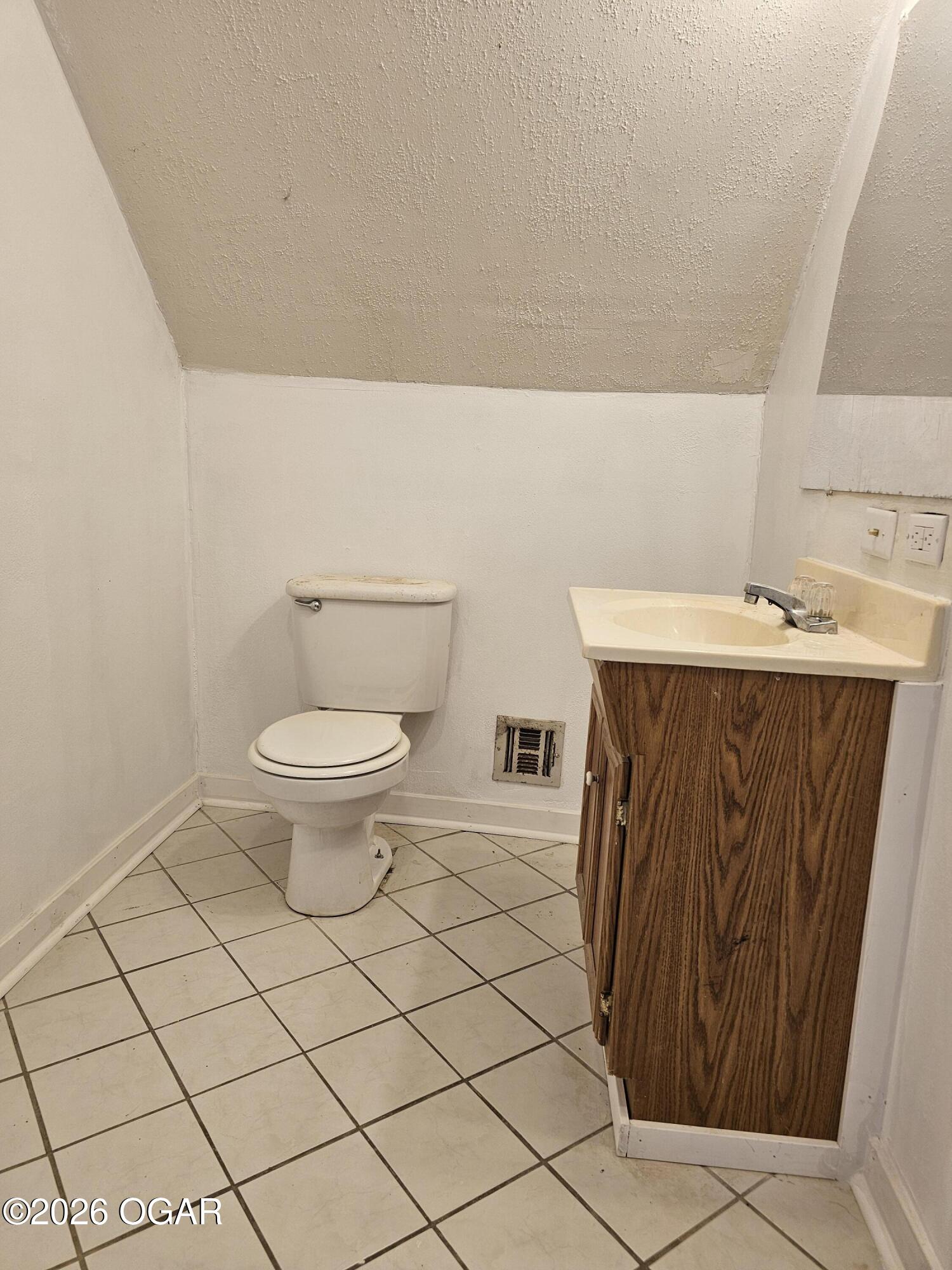 Bathroom with tiled floor, toilet, and wood-grain vanity beneath a sloped ceiling.