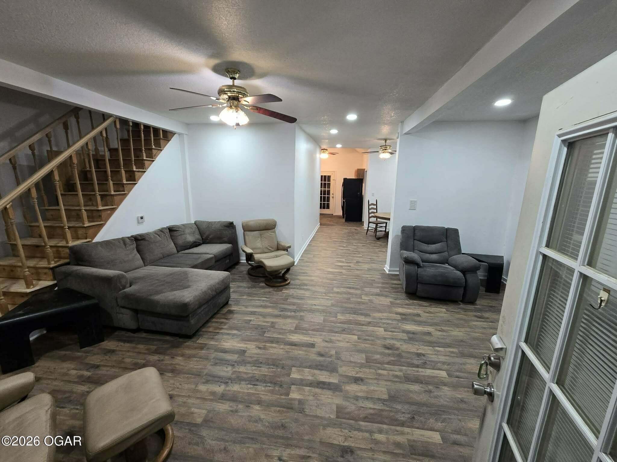 Furnished living room with gray sectional, wood-look floors, and staircase along the left wall.
