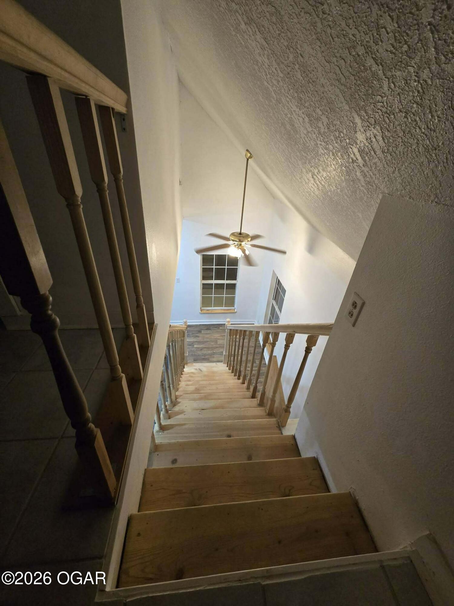 Wooden staircase descending into a two-story room with a vaulted ceiling and large window.