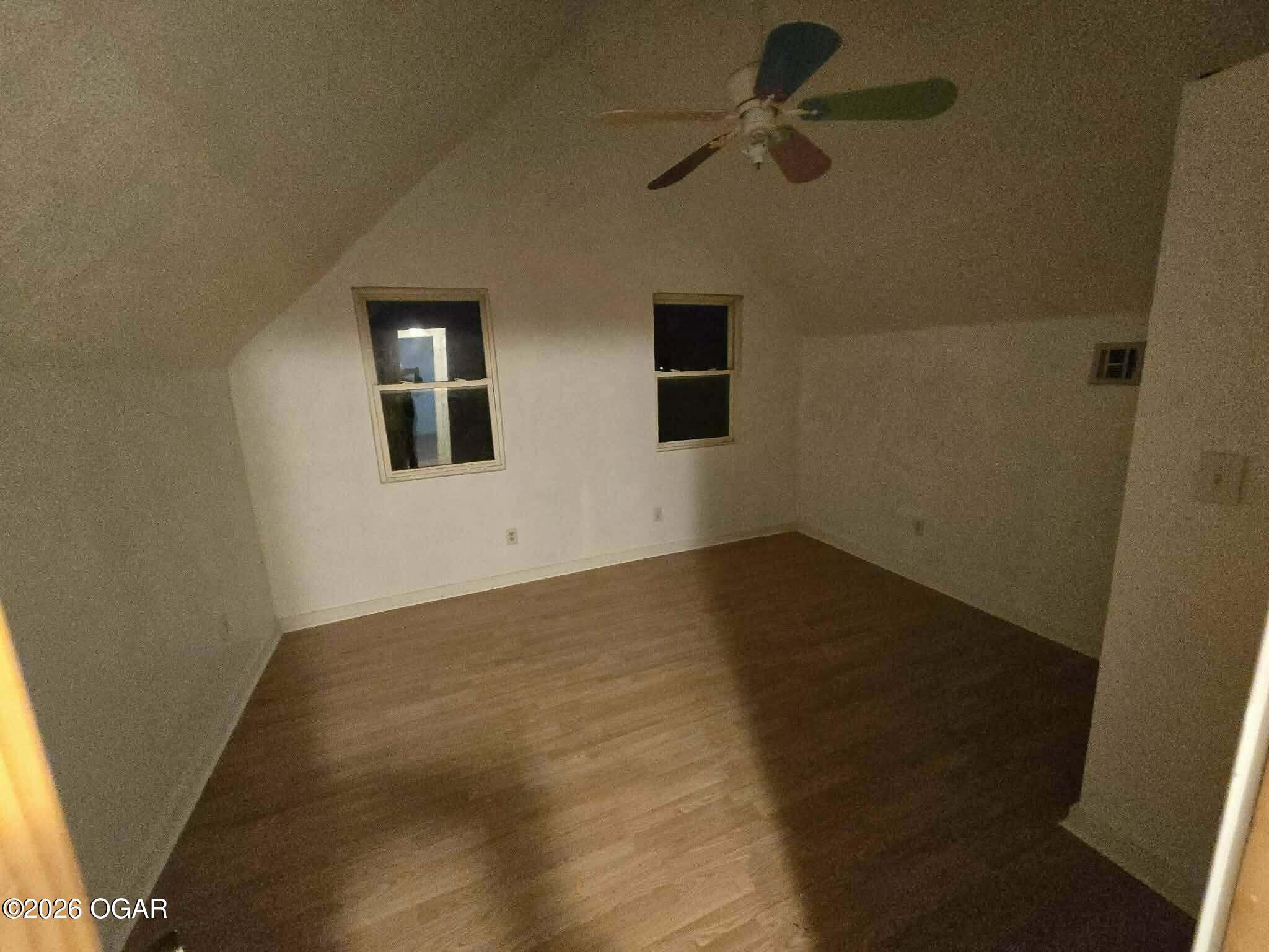 Empty room with wood-look flooring, two windows, and a ceiling fan.