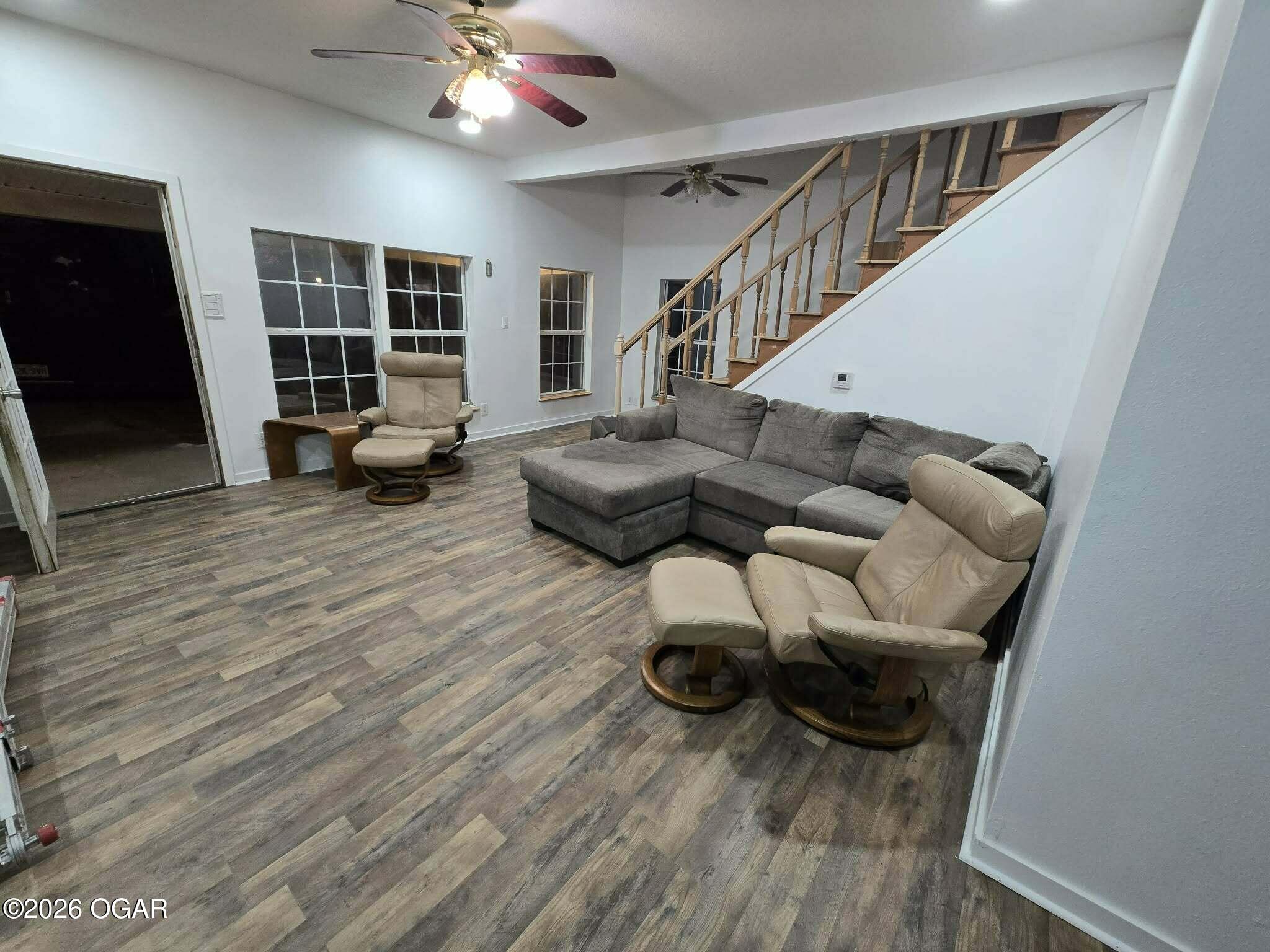 Living room with a gray sectional, beige recliners, and an open staircase.