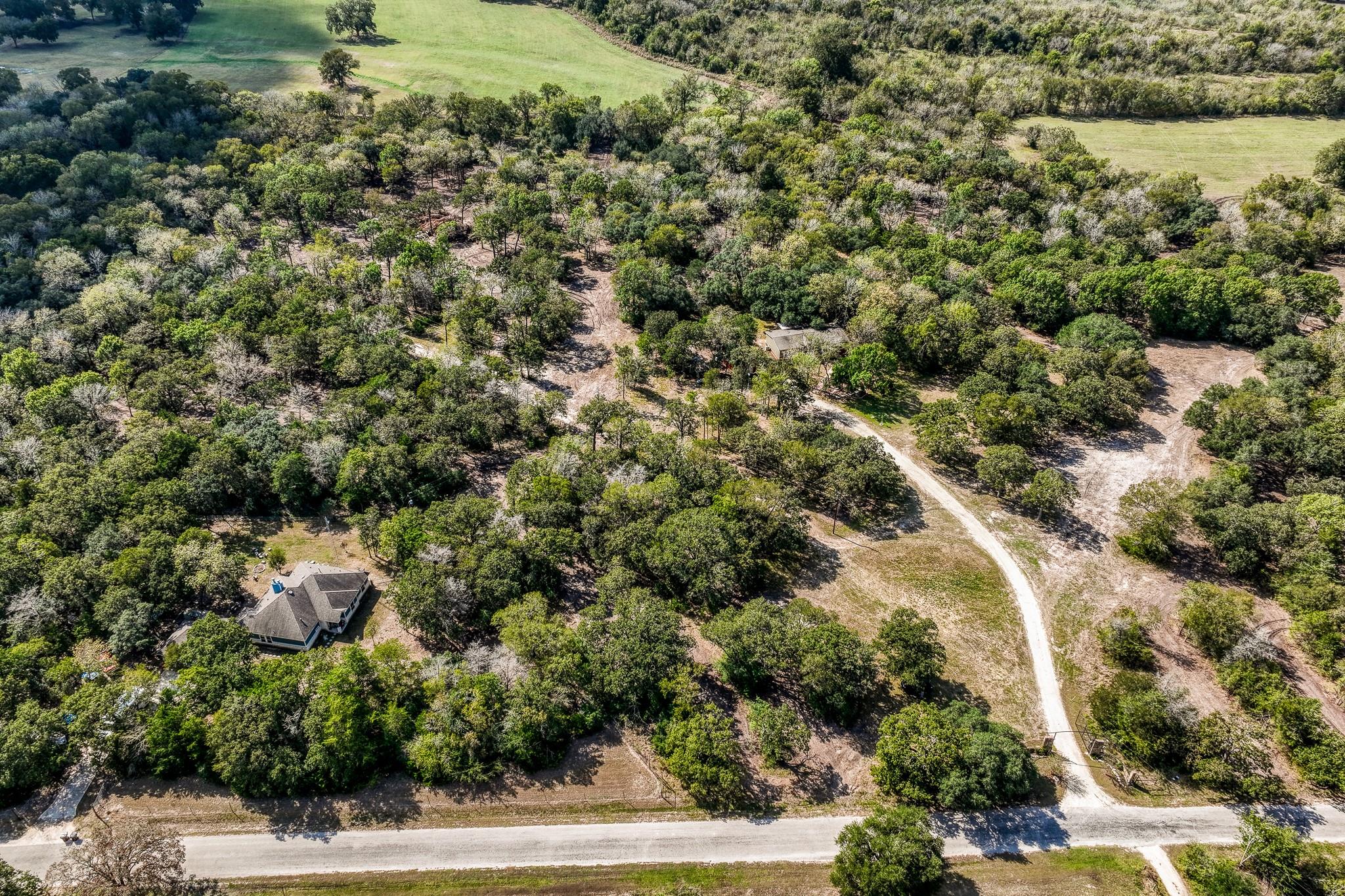 Aerial view of wooded acreage with a house, open clearings, and a curved gravel drive.