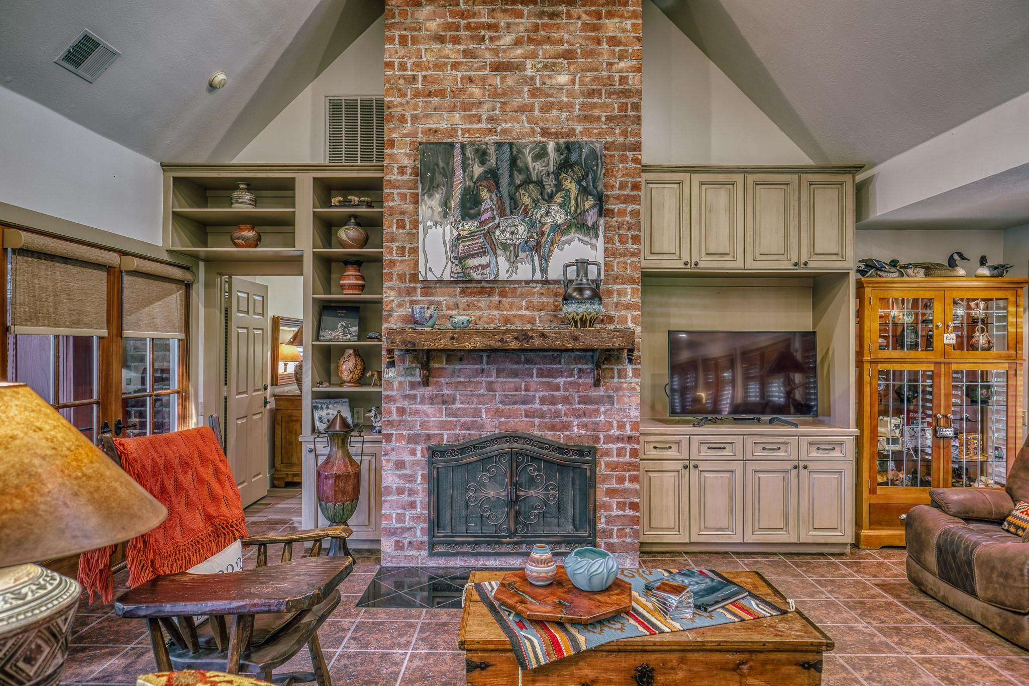 Living room with a tall brick fireplace, built-in cabinetry, and rustic wood furniture.