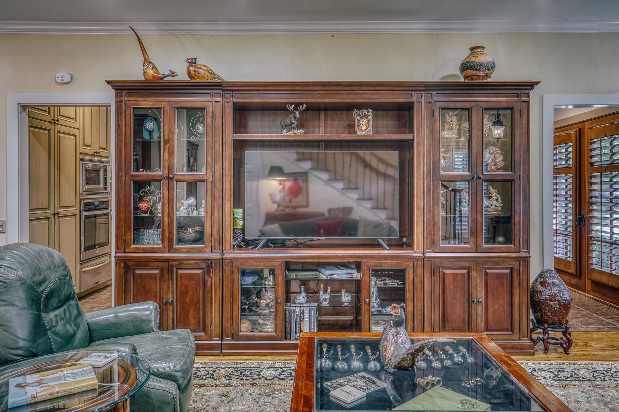 Living room with a large built-in wood entertainment center, leather armchair, and glass coffee table.