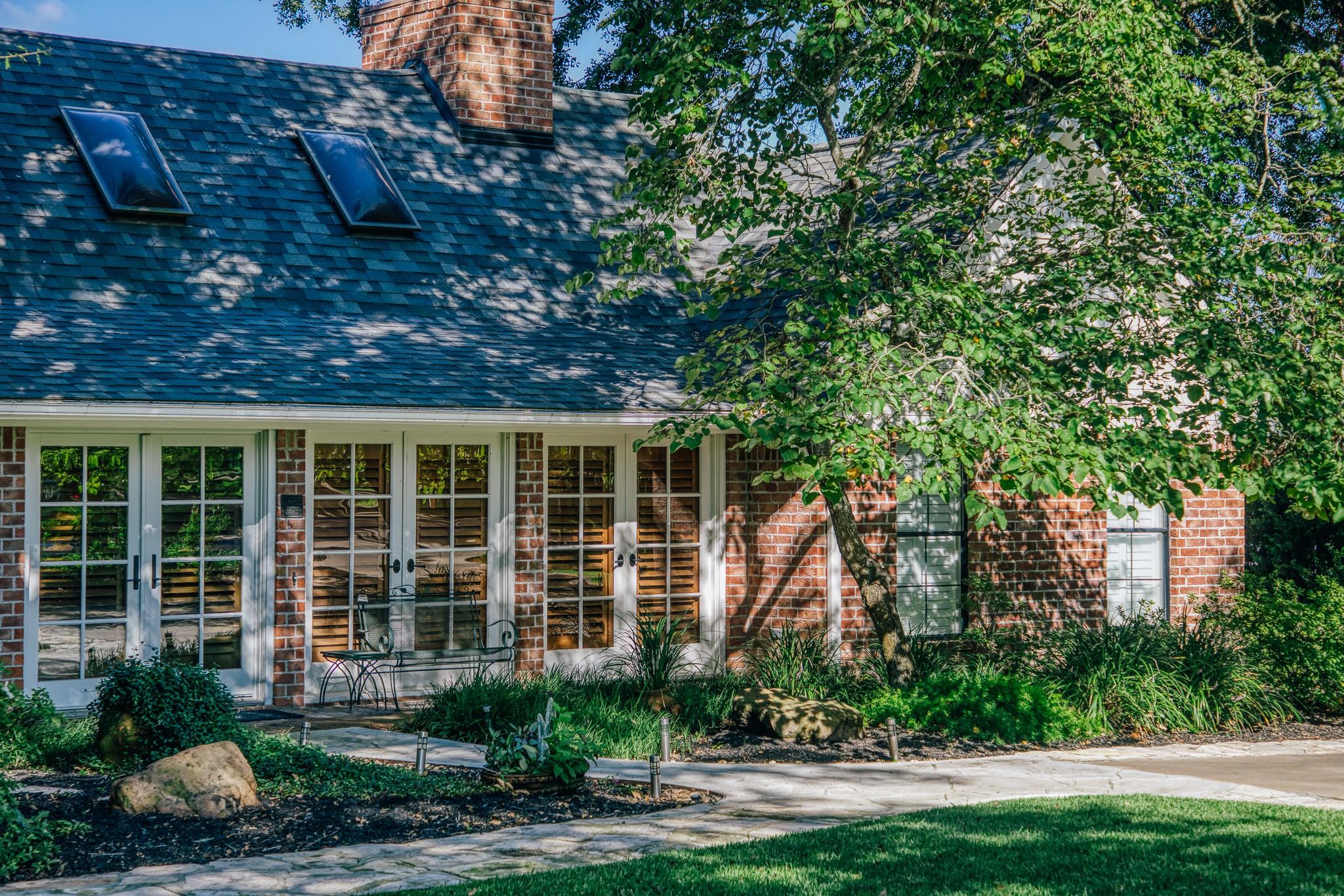 Brick house exterior with skylights, glass doors, and a shaded garden bench.