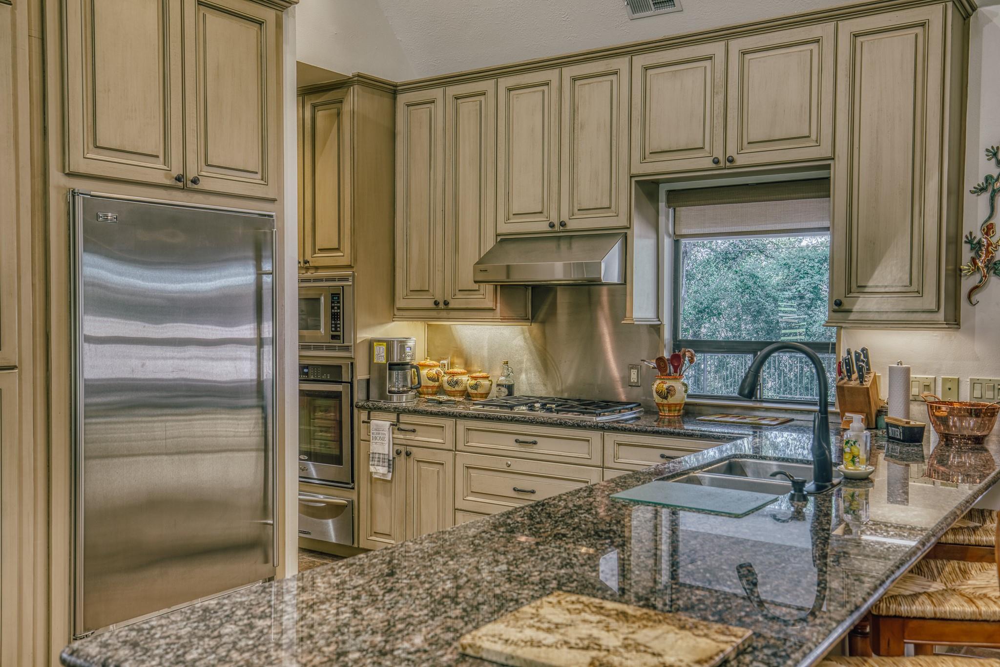 Kitchen with paneled wood cabinets, granite counters, stainless appliances, and a large island sink.