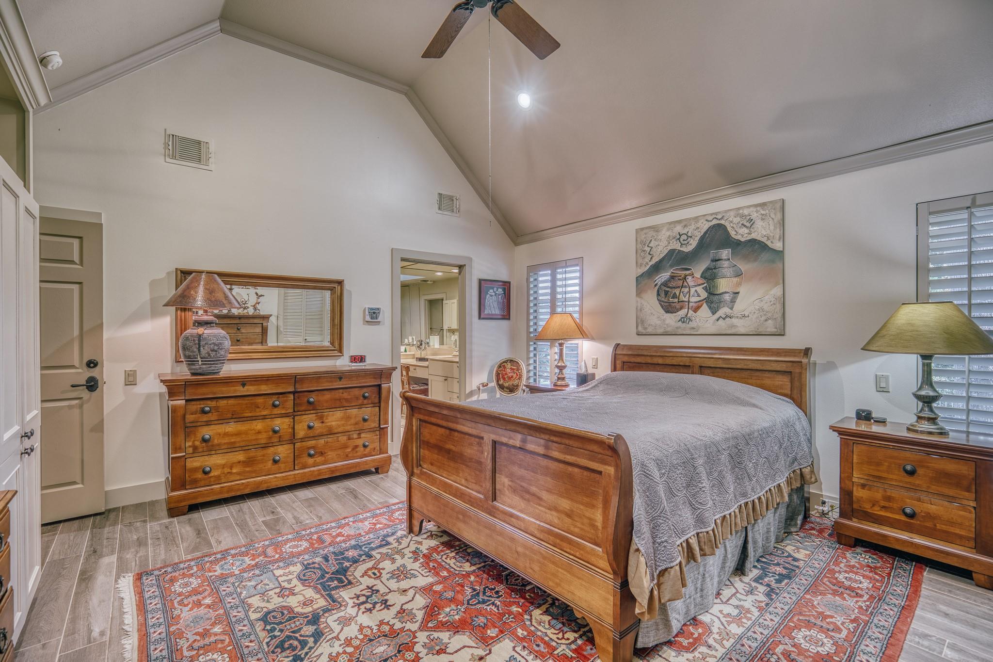 Bedroom with a vaulted ceiling, wooden furnishings, patterned rug, and doorway to the bathroom.