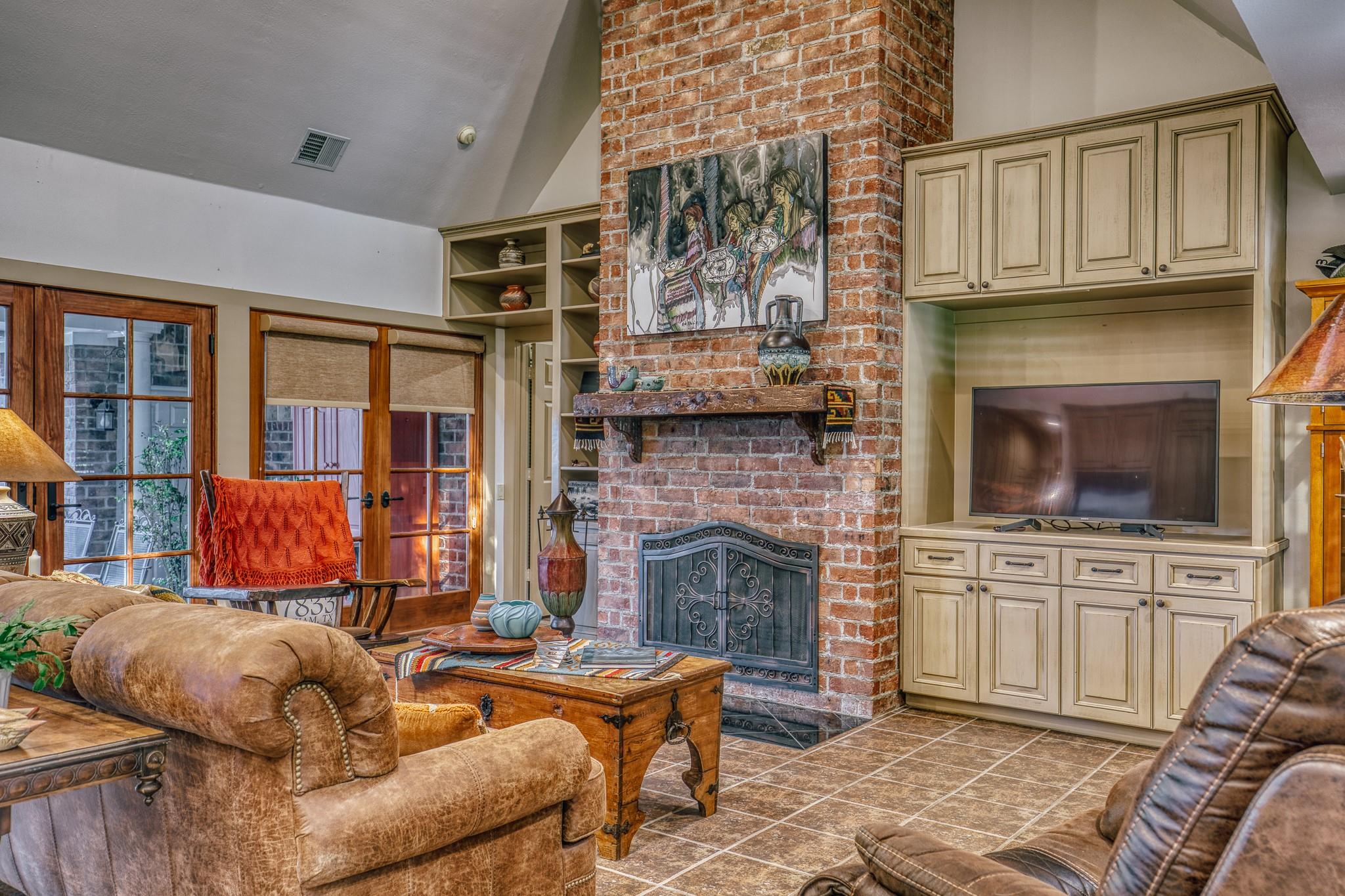 Living room with a brick fireplace, built-in television cabinetry, French doors, and leather seating.