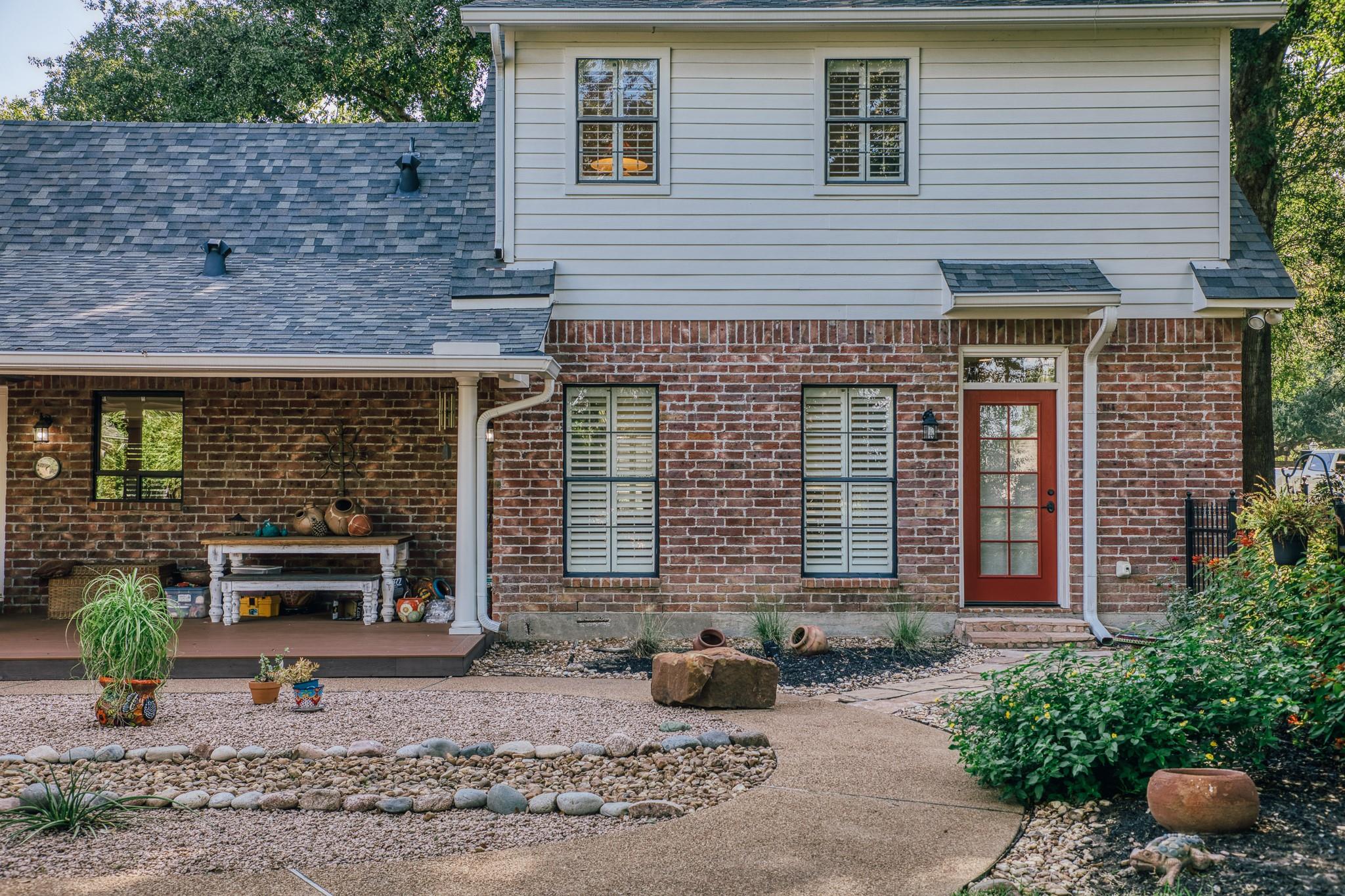 Two-story brick and siding home with a covered porch, red front door, and landscaped gravel garden.