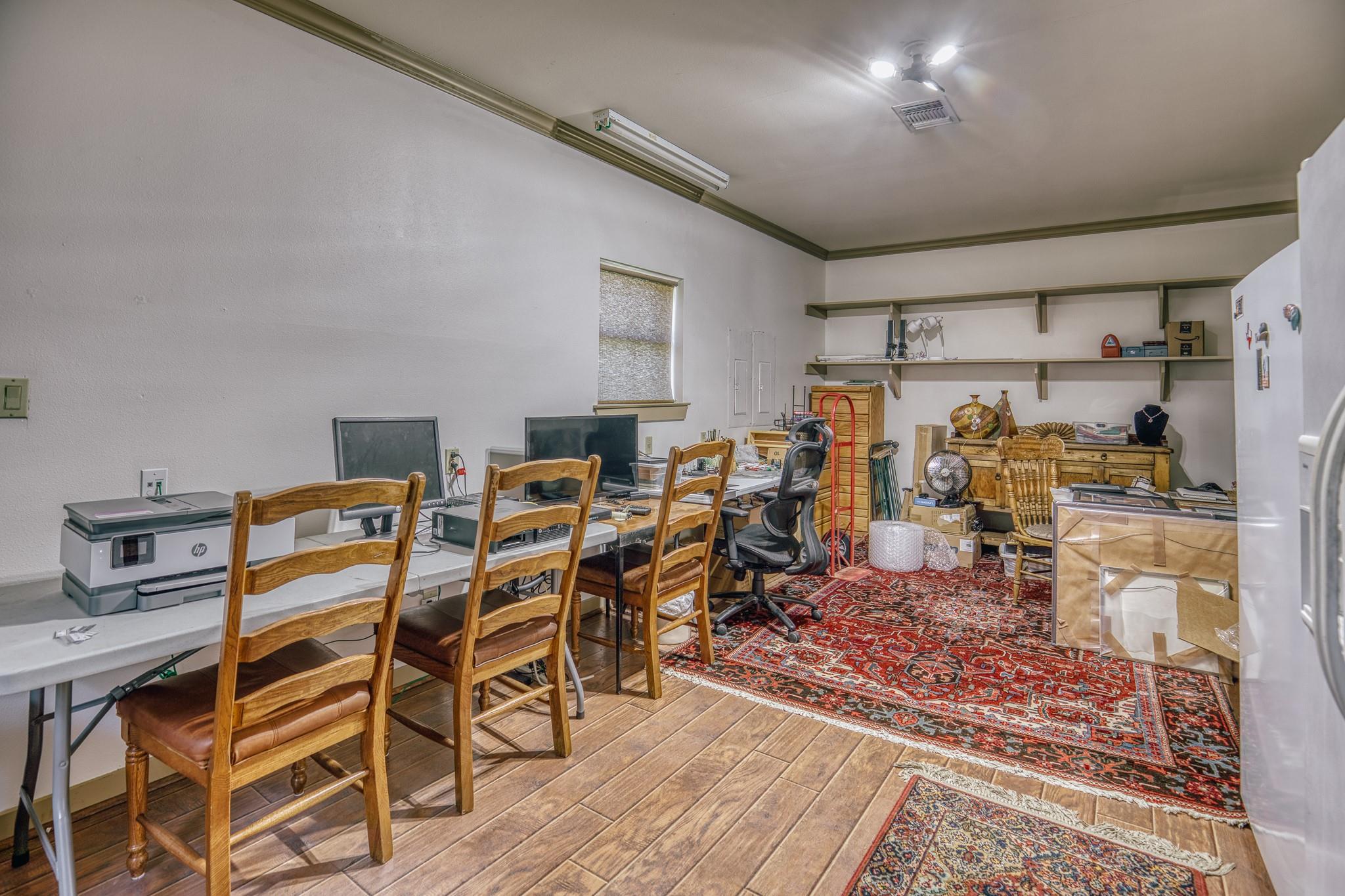 Office workroom with computer stations, wooden chairs, wall shelves, and red patterned rugs.