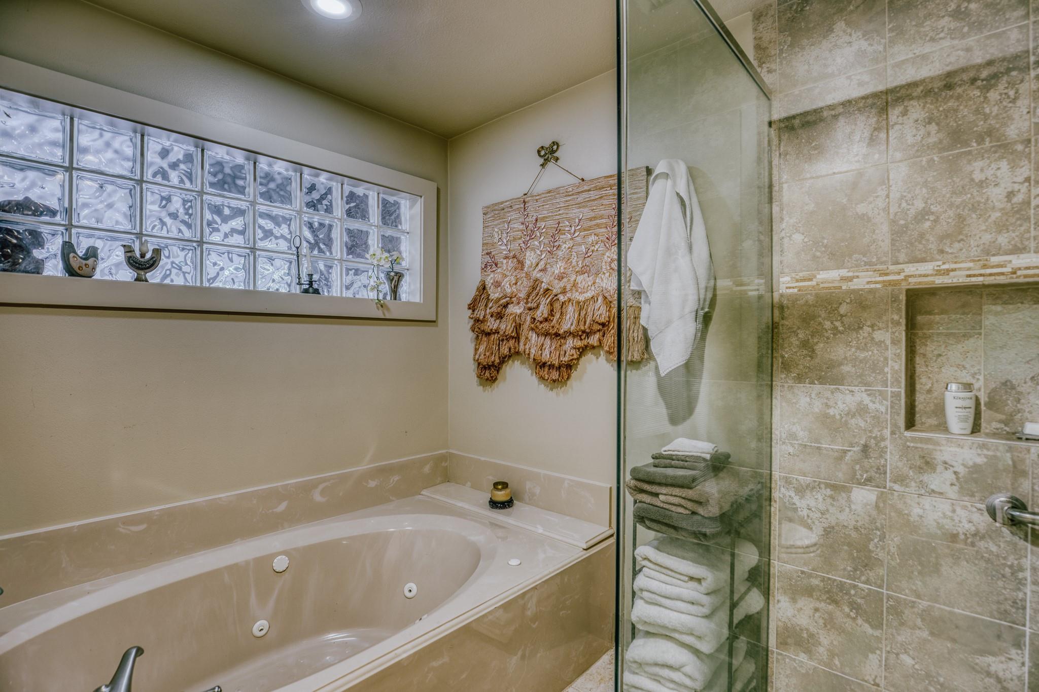 Bathroom with a jetted tub beneath a glass-block window and a stone-tile shower.