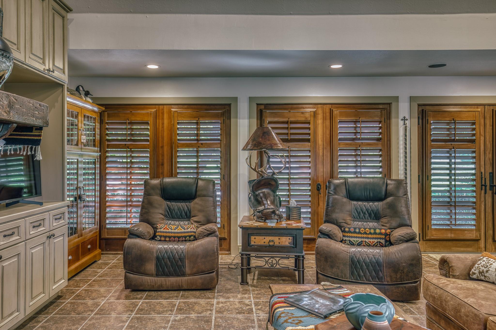 Living room with two leather recliners, wooden plantation shutters, and built-in television cabinetry.