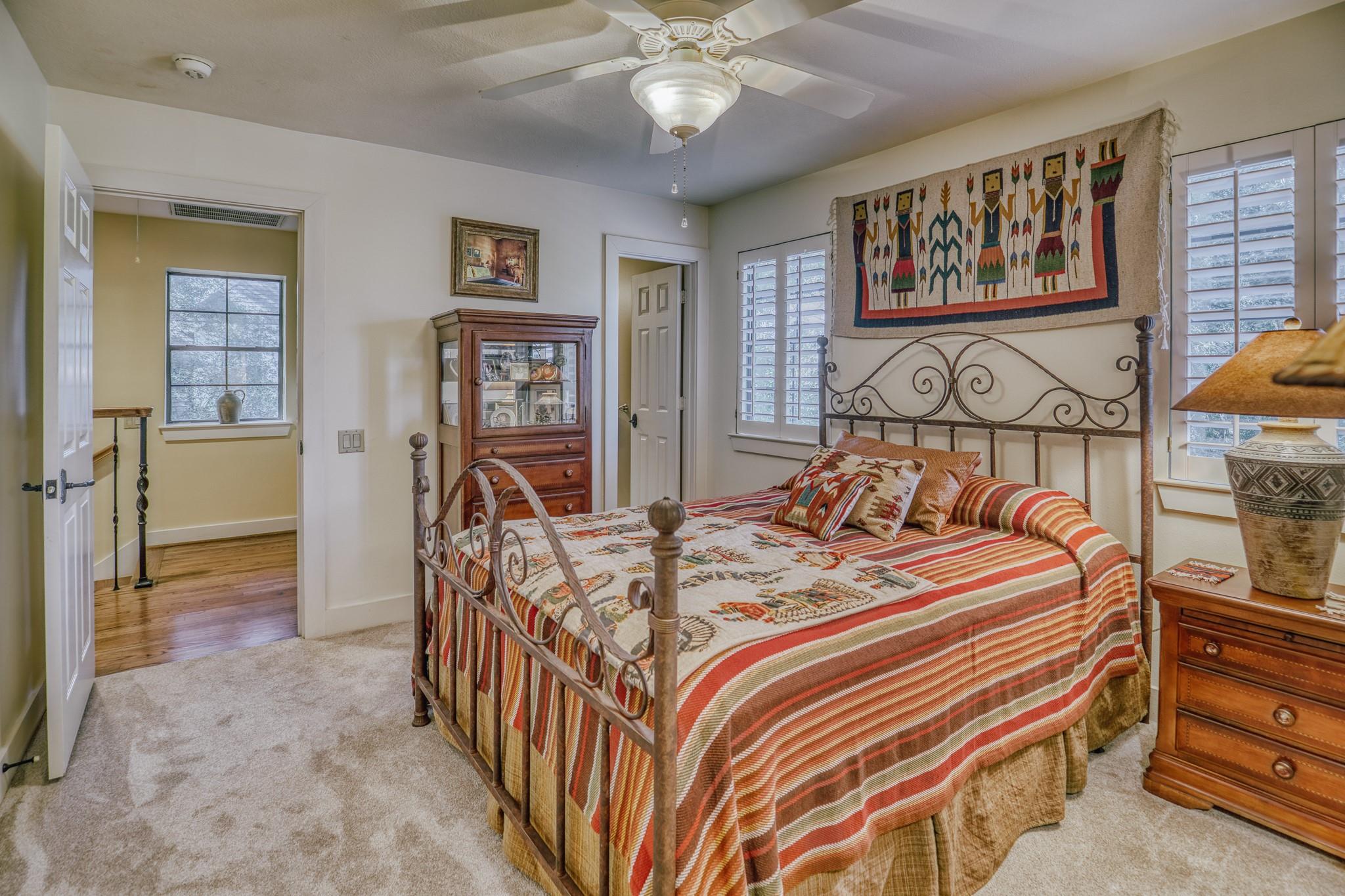 Bedroom with an ornate iron bed, striped quilt, shuttered windows, and wooden display cabinet.