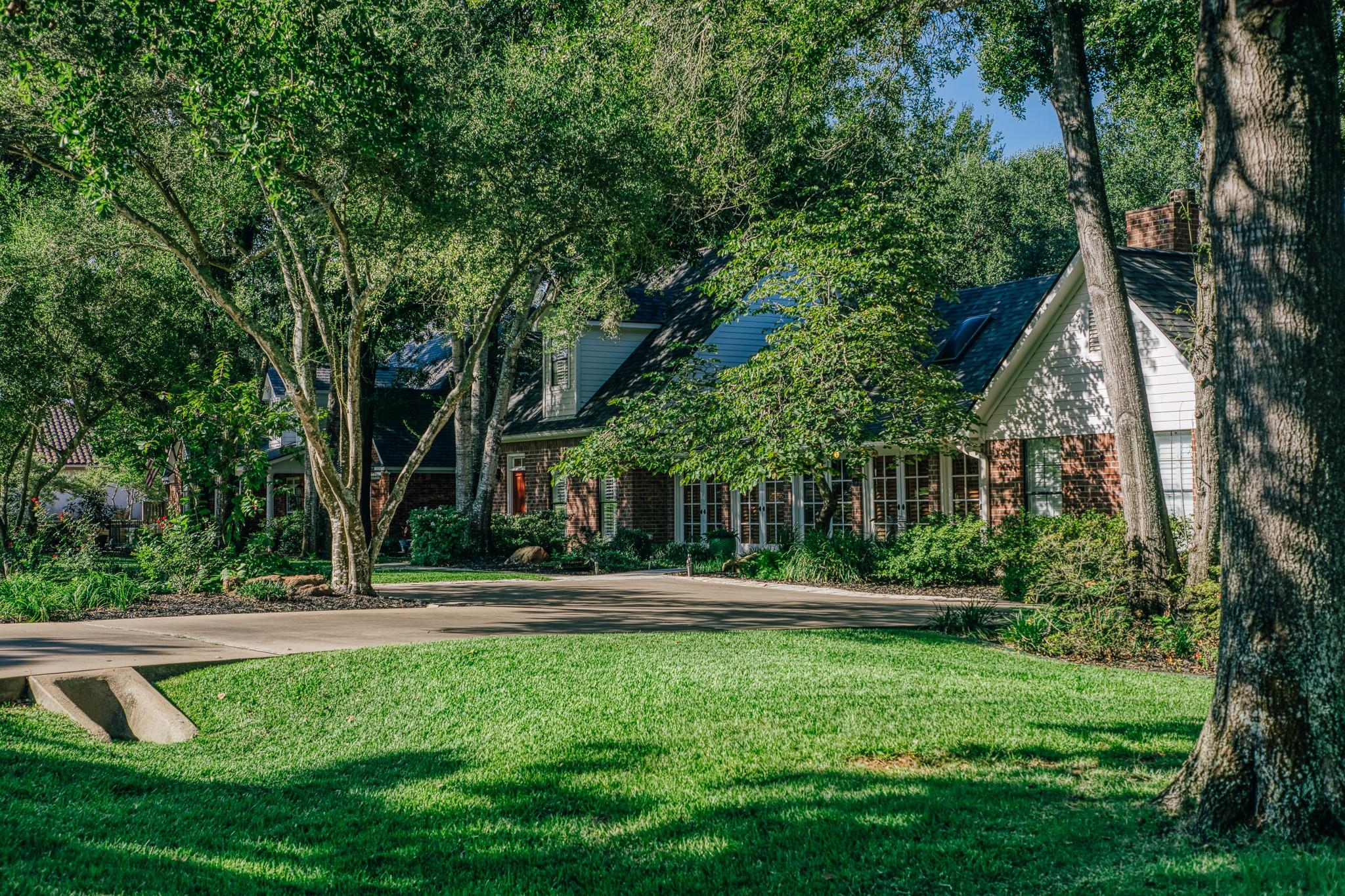 Two-story brick home nestled among mature trees, with a curved driveway and broad lawn.