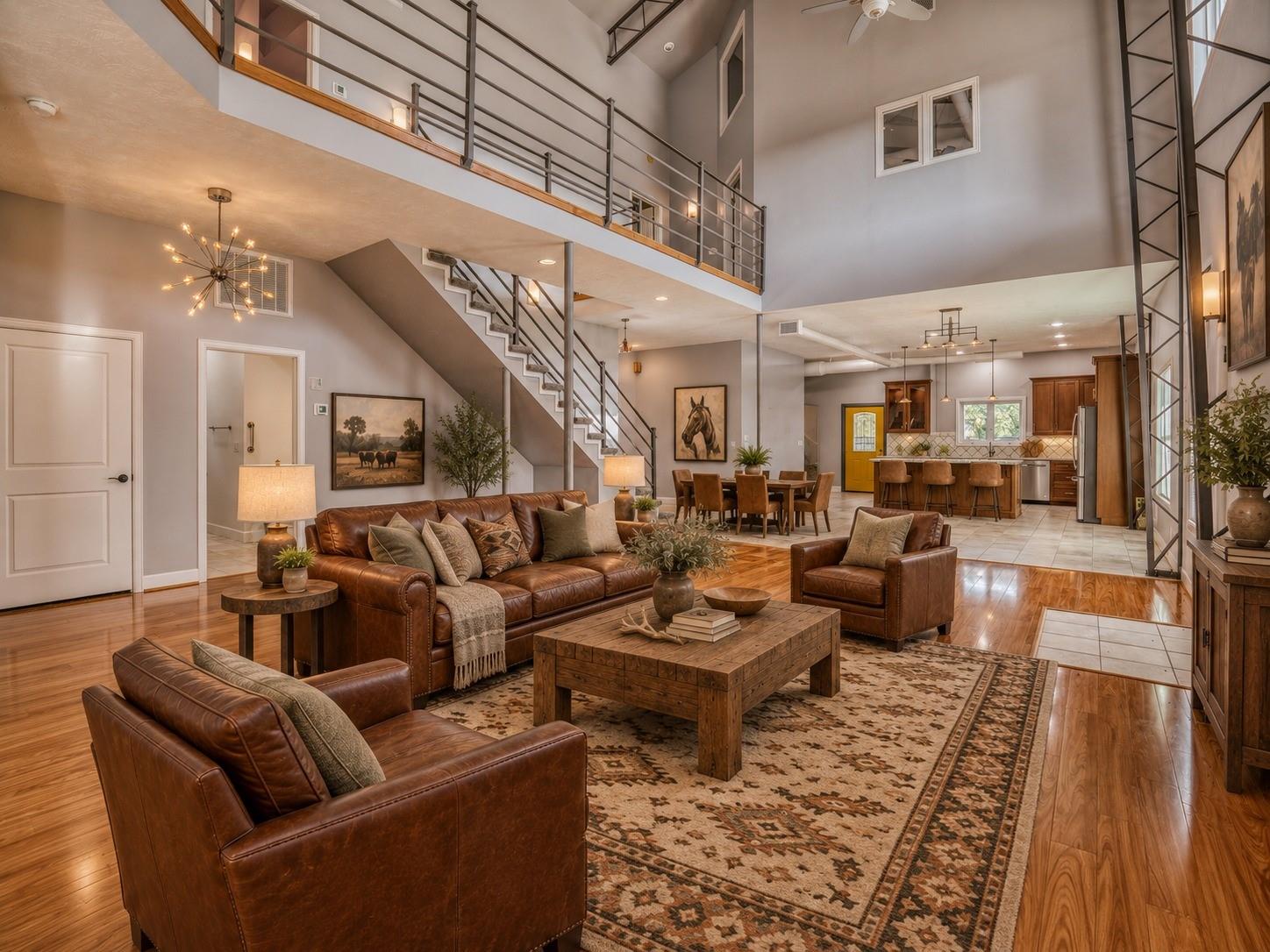 Double-height living room with leather sofas, a mezzanine balcony, staircase, and open kitchen and dining area.