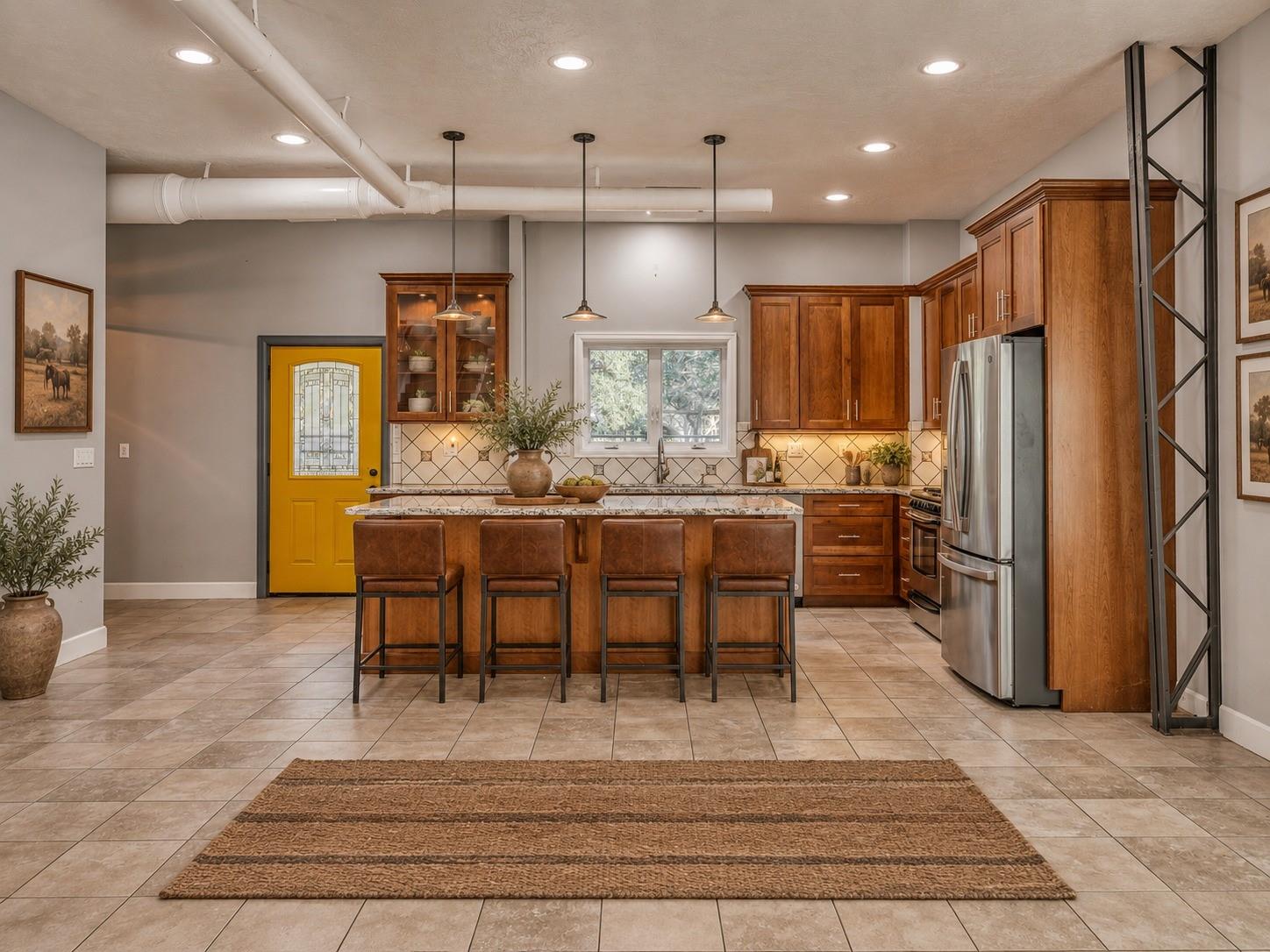 Kitchen with a wood-cabinet island, four leather stools, stainless appliances, and a bright yellow door.