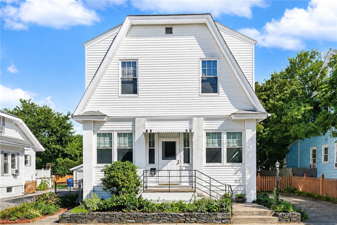White gambrel-roof house with a central entrance, black railings, and landscaped front garden.