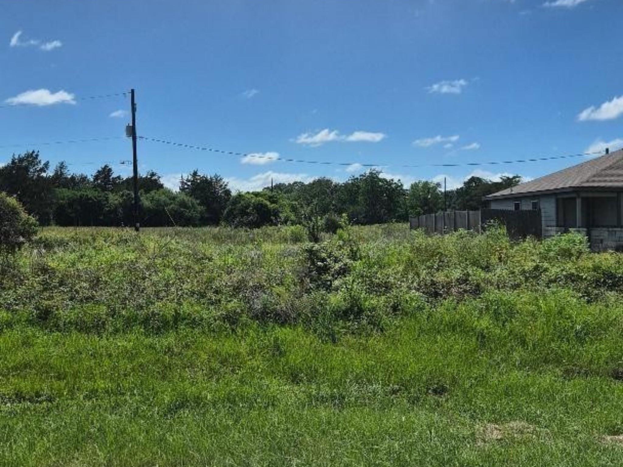 Vacant lot with tall grass, a utility pole, and a neighboring house.