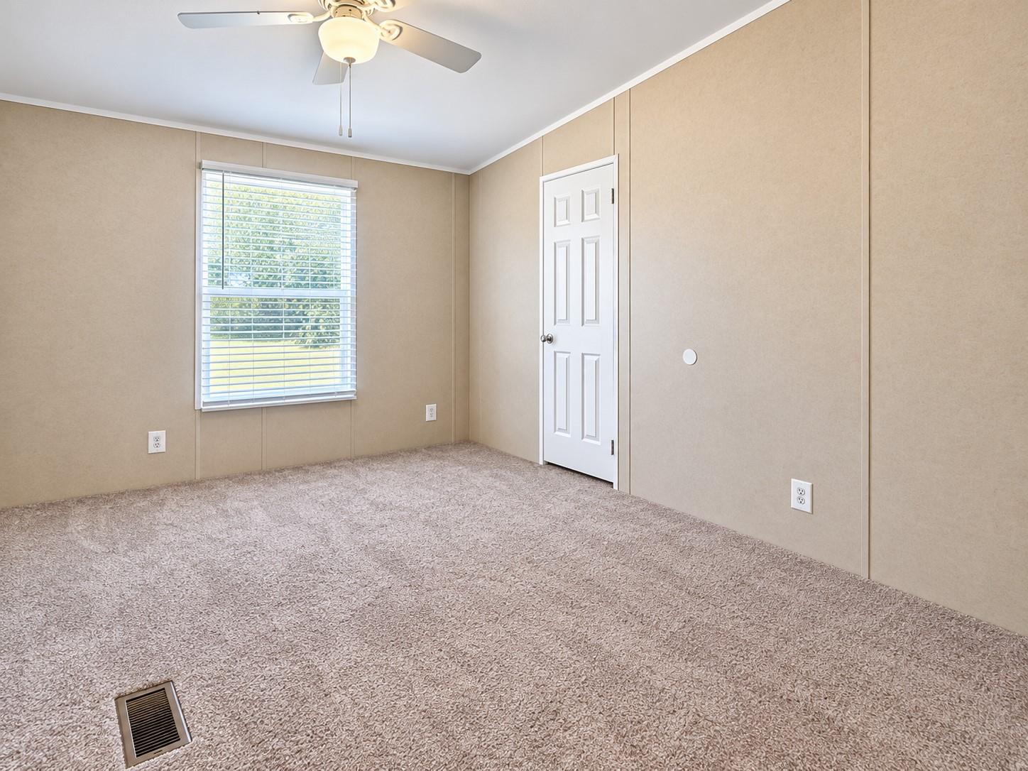 Empty bedroom with beige walls, light carpet, a window with blinds, and a ceiling fan.