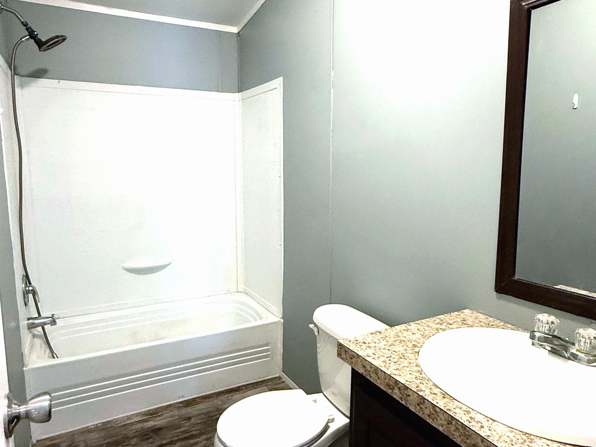 Bathroom with a white tub and shower, toilet, and dark vanity with a speckled countertop.