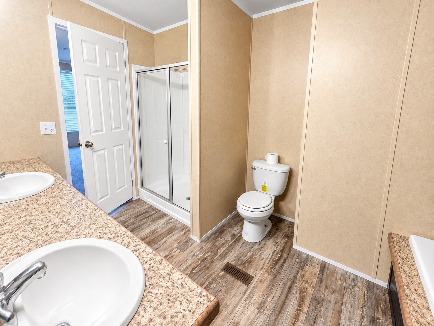 Bathroom with a glass-enclosed shower, two sink vanities, and wood-look flooring.