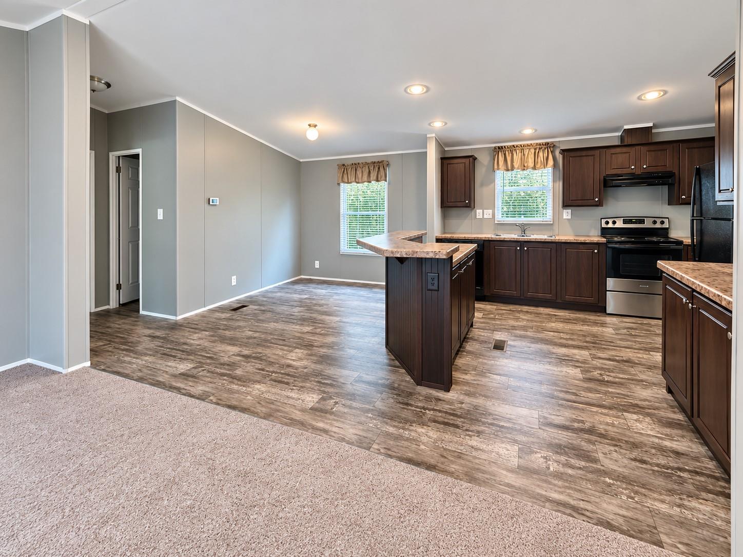 Unfurnished kitchen with dark cabinets, a central island, stainless steel appliances, and adjoining carpeted space.