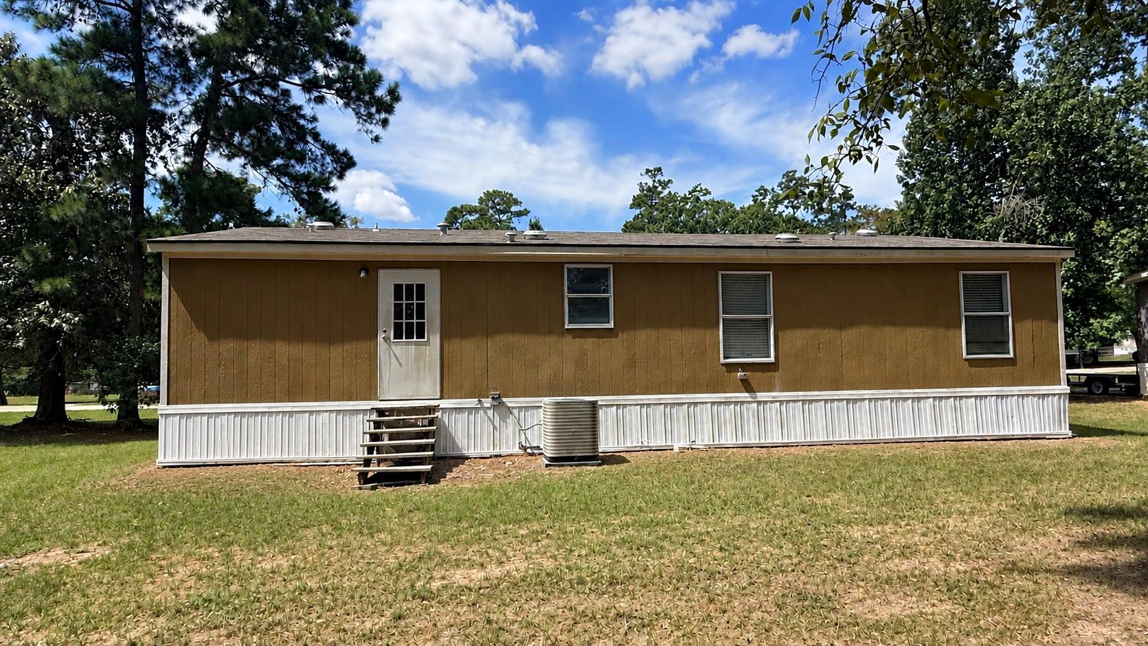 Single-story manufactured home with brown siding, white lower skirting, and a grassy yard.