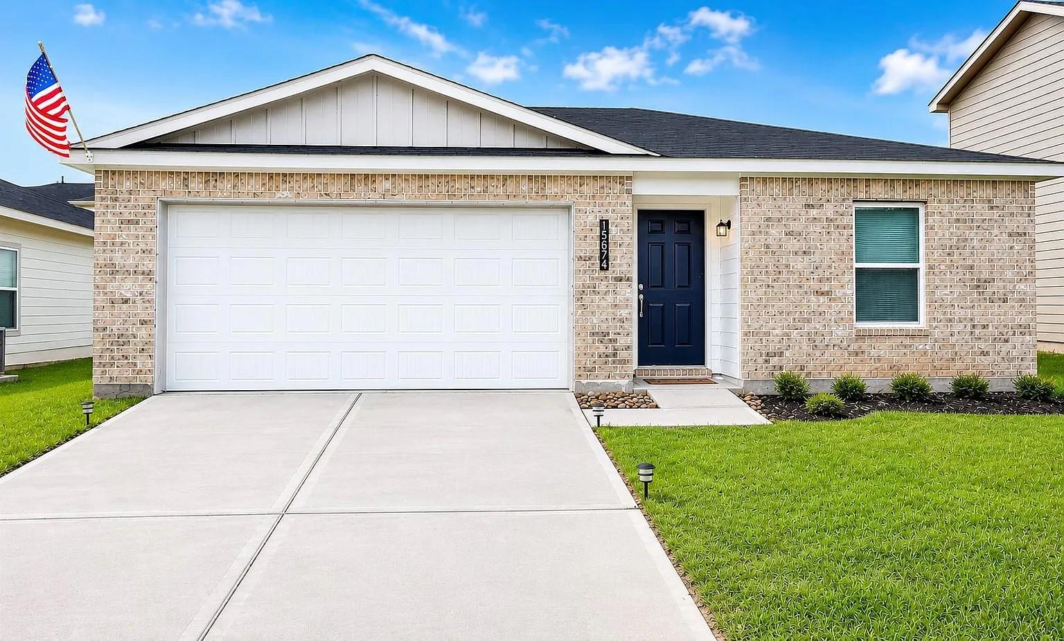Single-story brick home with a white double garage, navy entry door, and American flag.