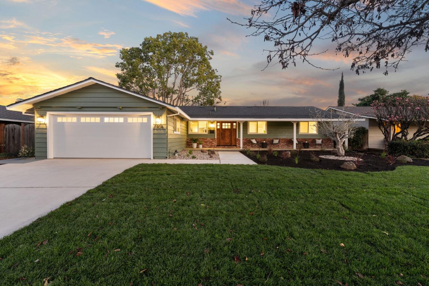 Single-story ranch home with a covered porch and two-car garage at dusk.