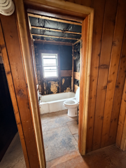 Wood-paneled bathroom viewed through a doorway, with a toilet and small window.