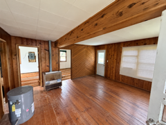 Wood-paneled room with hardwood floors, exposed beam, windows, a chair, and a portable heater.