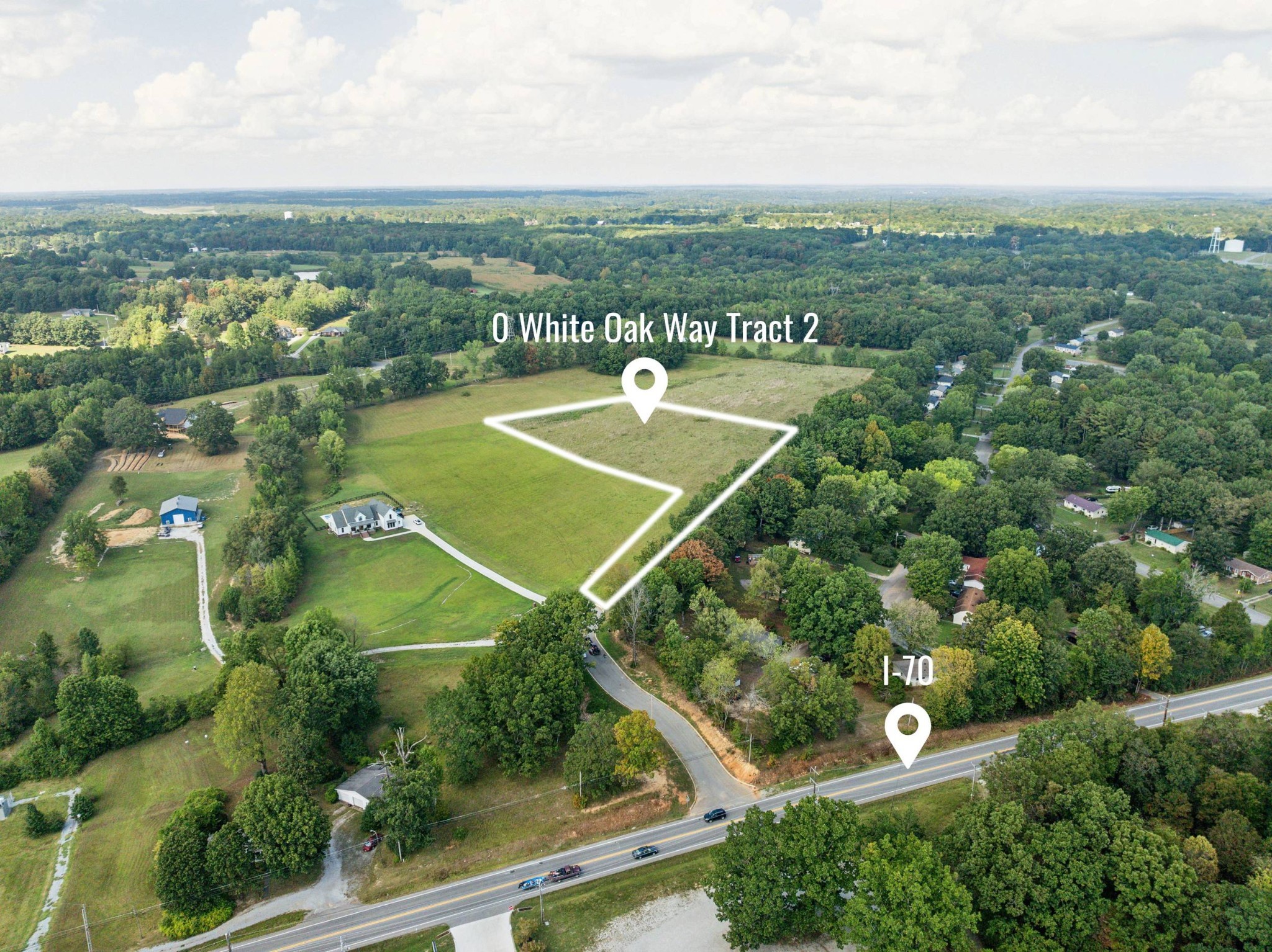 Aerial view of a marked vacant land tract surrounded by fields, trees, and nearby homes.