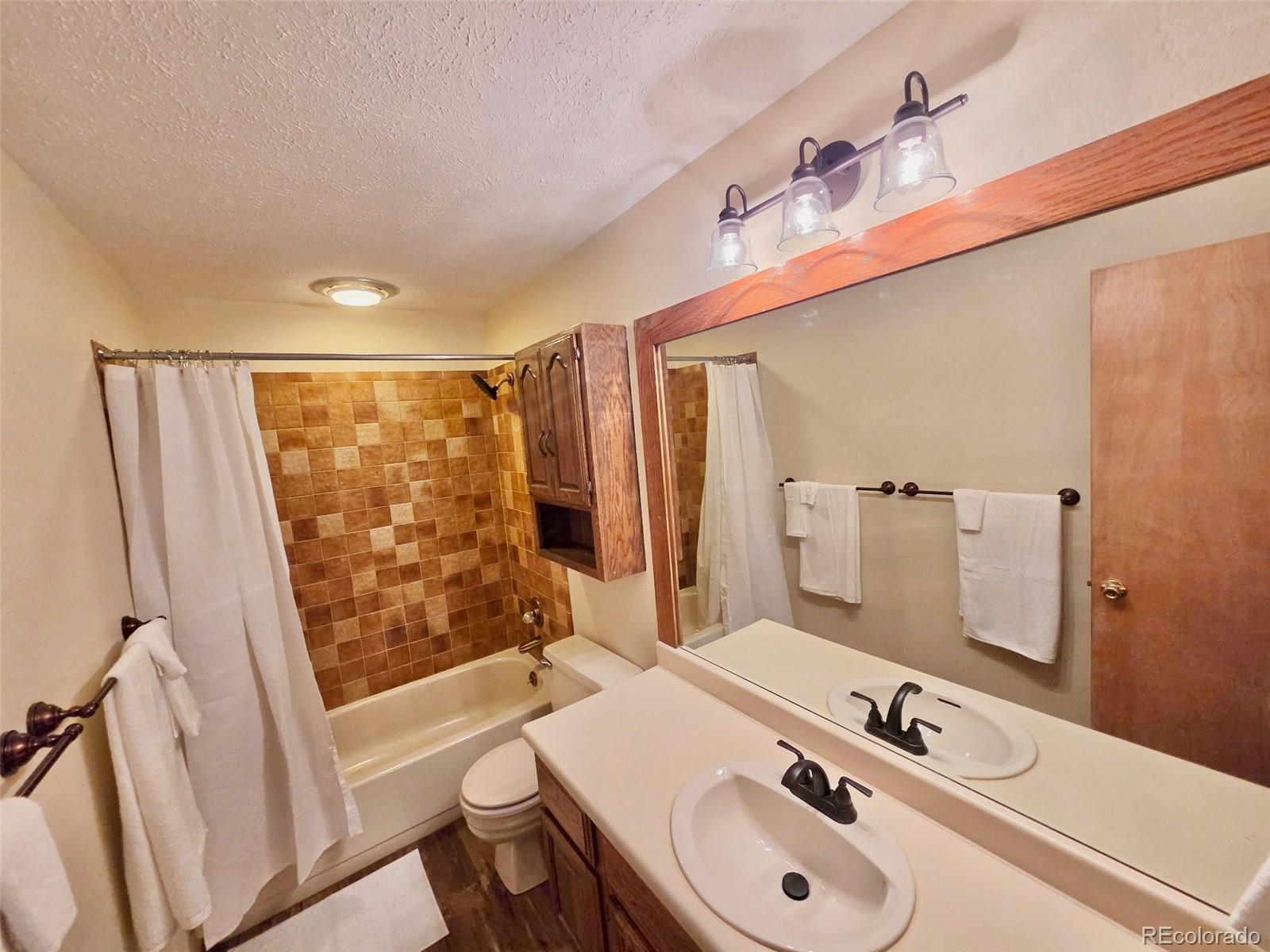 Bathroom with tiled tub and shower, wood-framed mirror, and double-sink vanity.