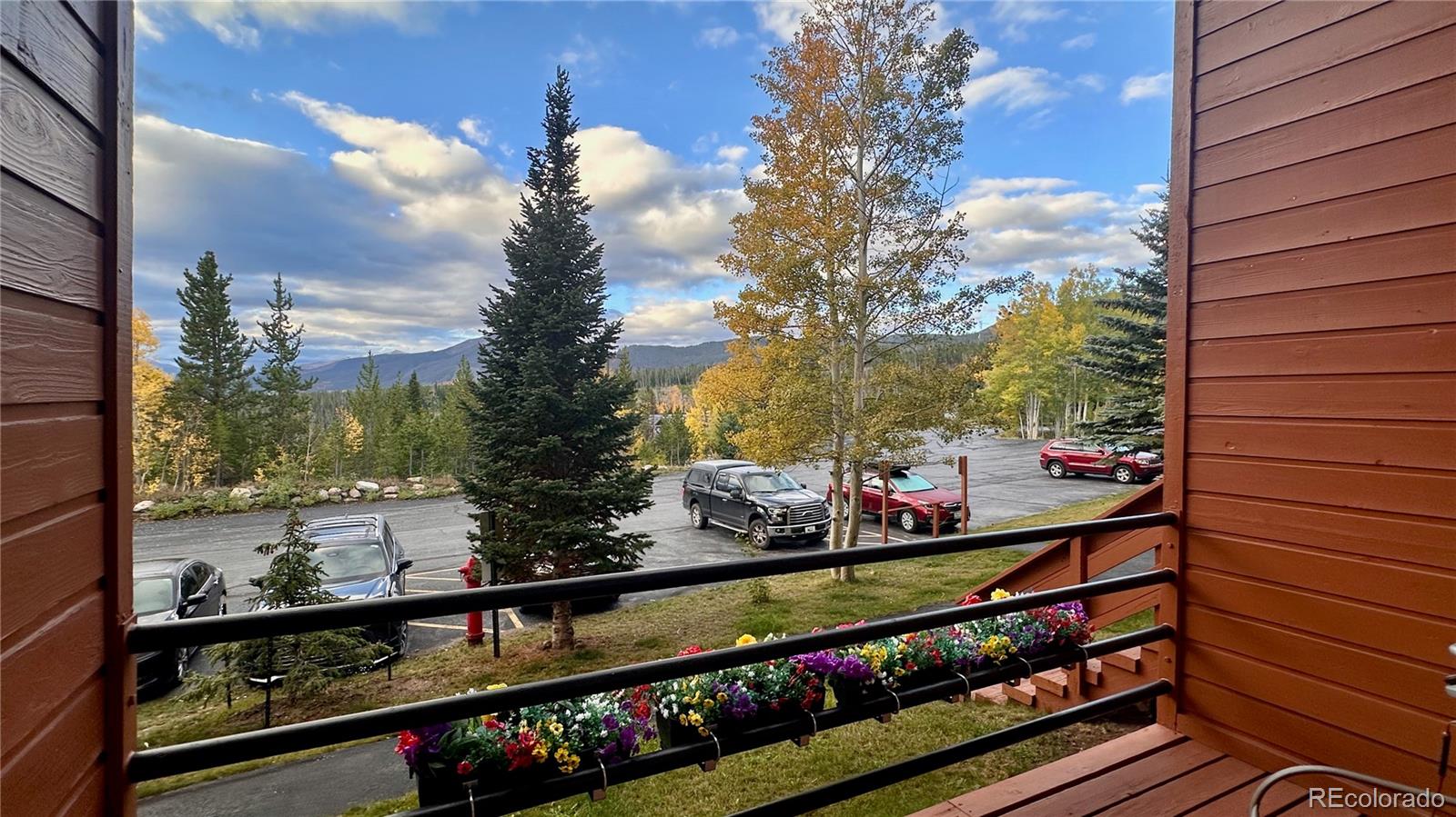 Balcony view of autumn-colored trees, mountains, and a parking area beyond flower boxes.