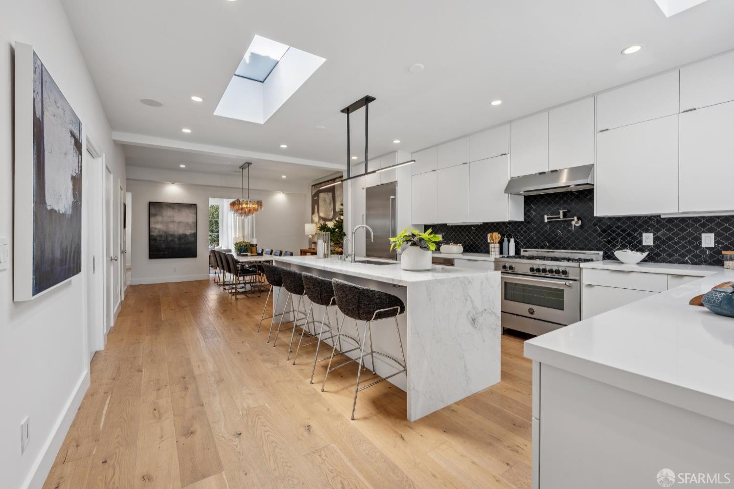 Modern kitchen with marble island, black tile backsplash, and skylight opening to a dining area.