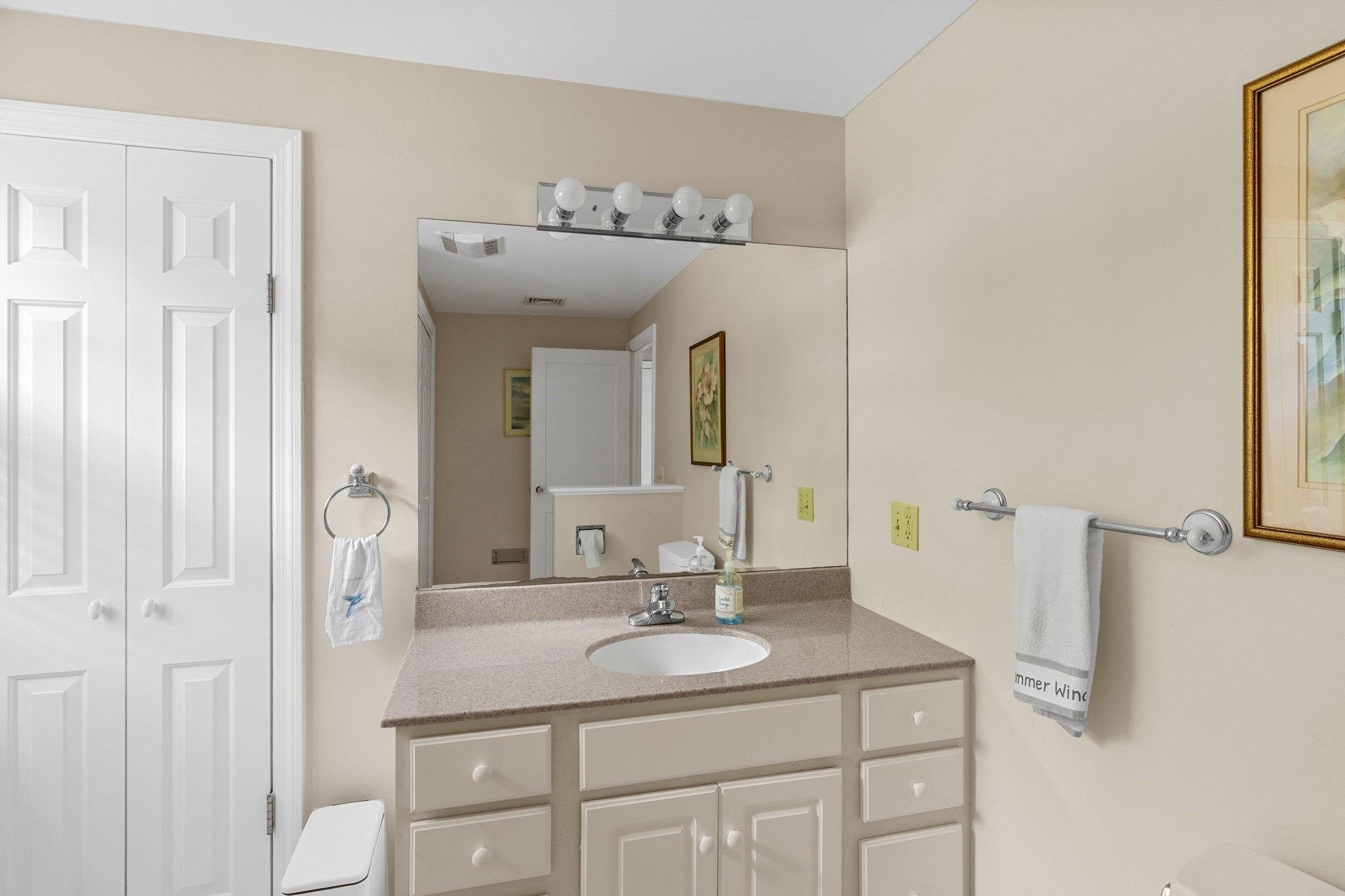 Bathroom vanity with an oval sink, cream cabinetry, large mirror, and white towels.